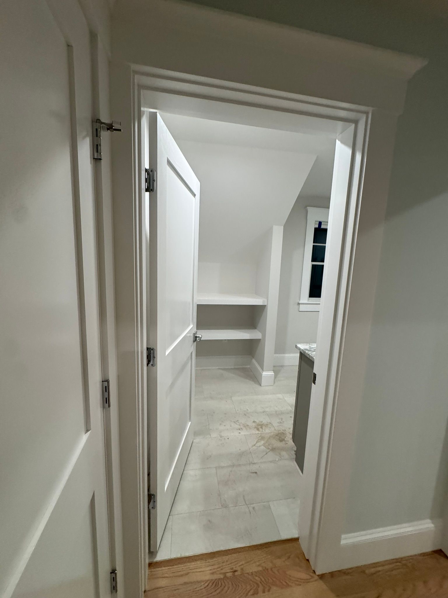 Open doorway to a bright, empty room with white walls, built-in shelves, and a window.