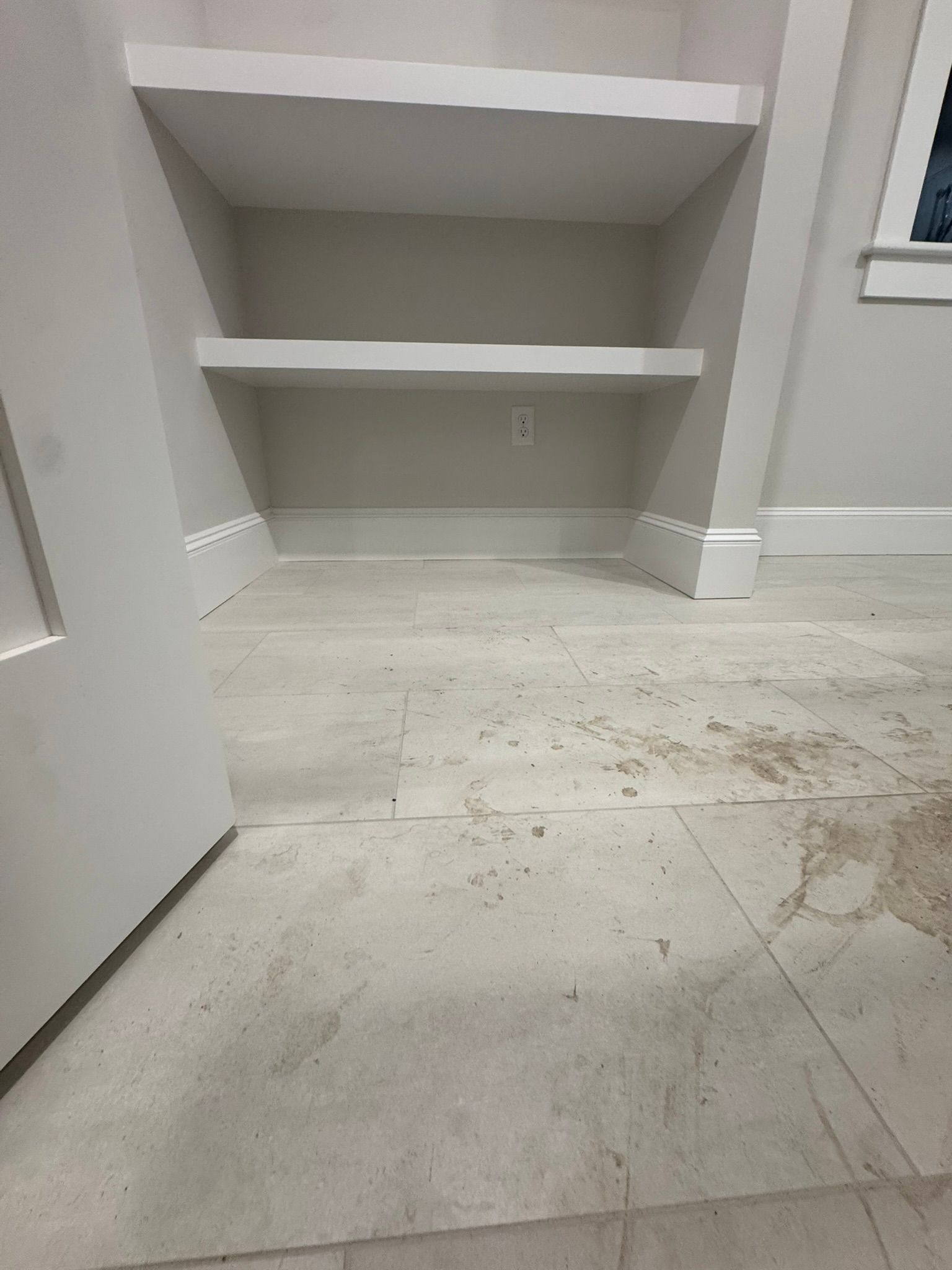Empty white closet with built-in shelves and a dusty floor, viewed from the doorway