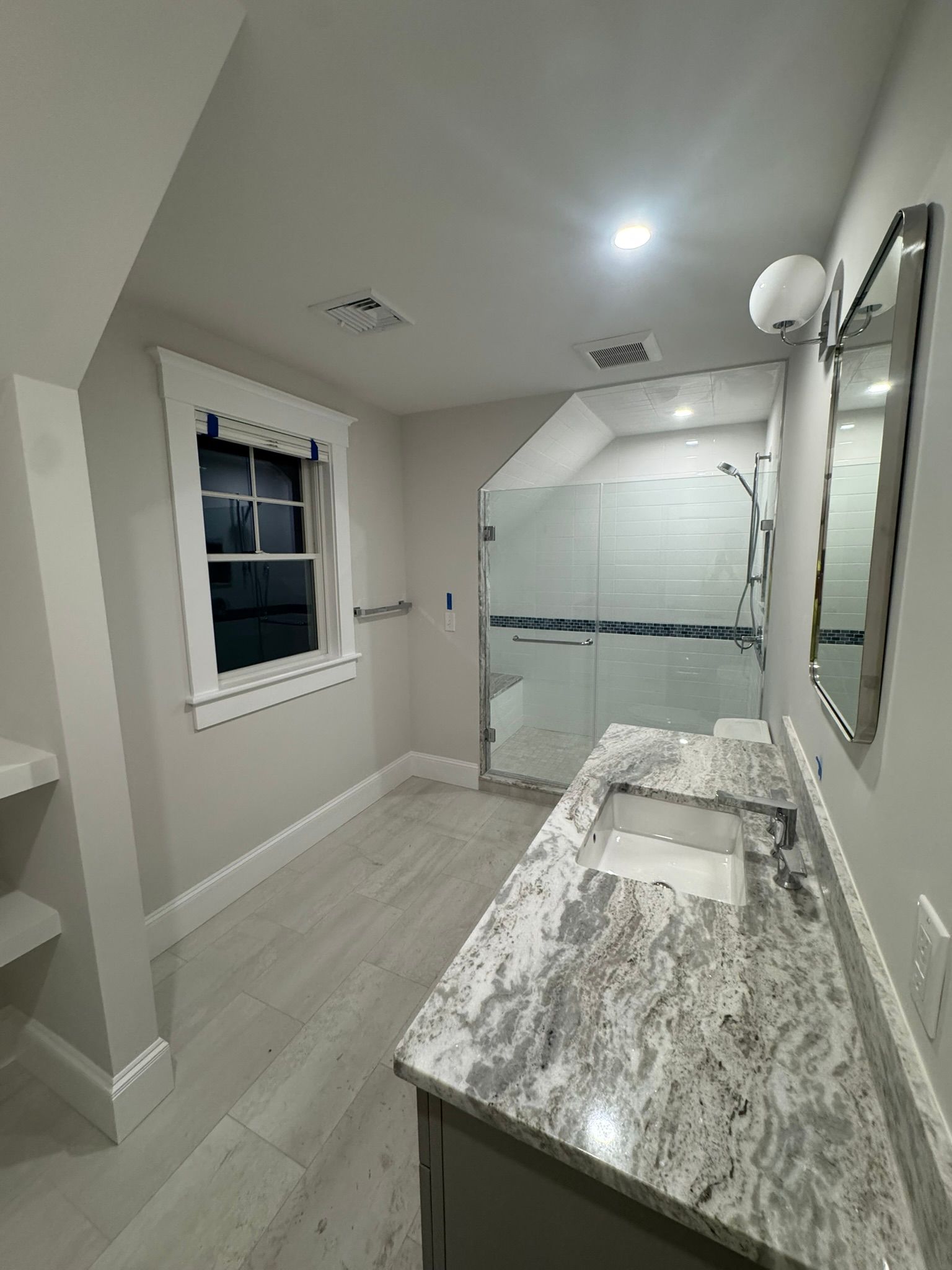 Modern bathroom with granite vanity, large mirror, and glass walk-in shower.