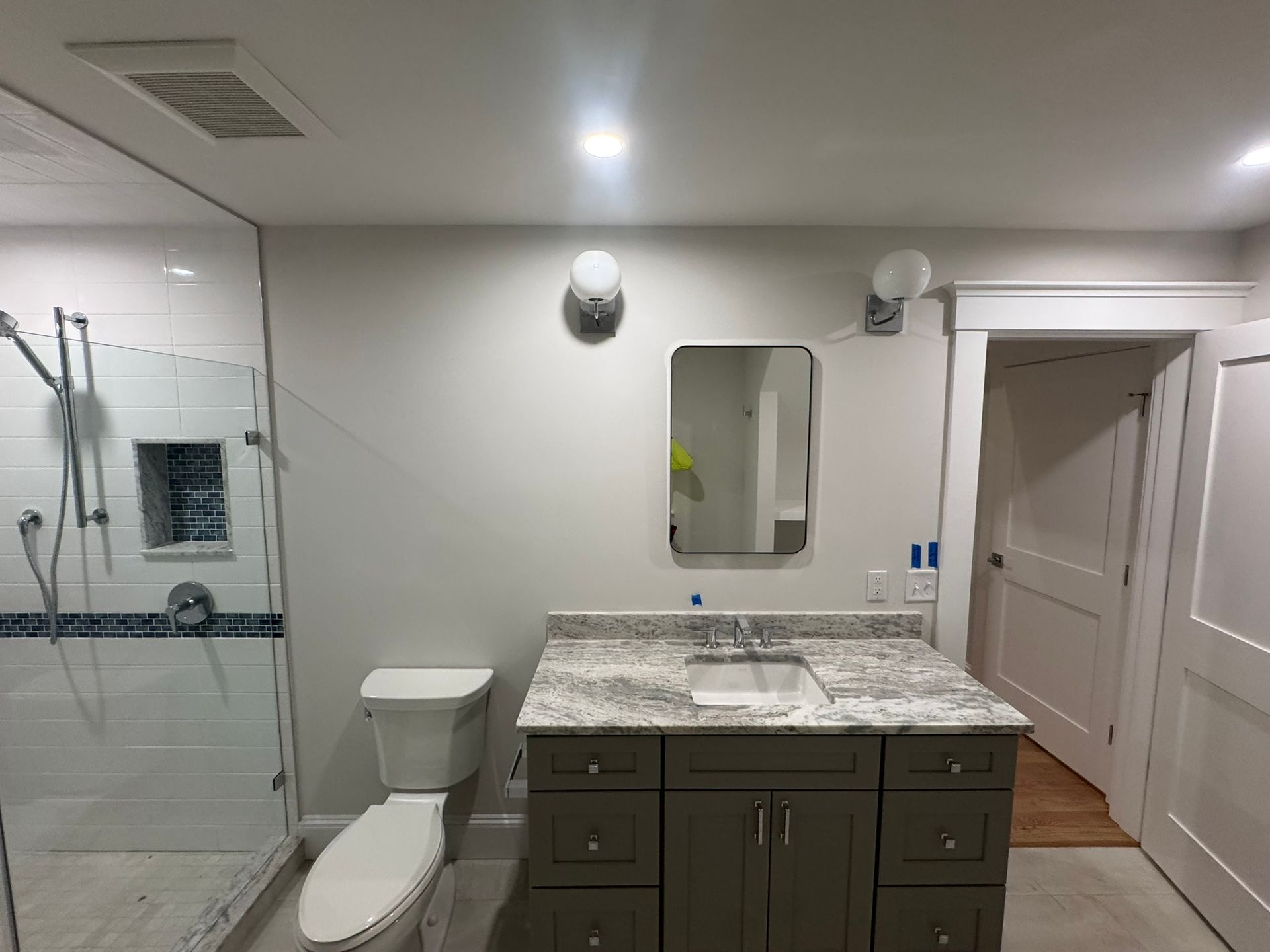 Modern bathroom with glass shower, toilet, and dark vanity with granite countertop and mirror.