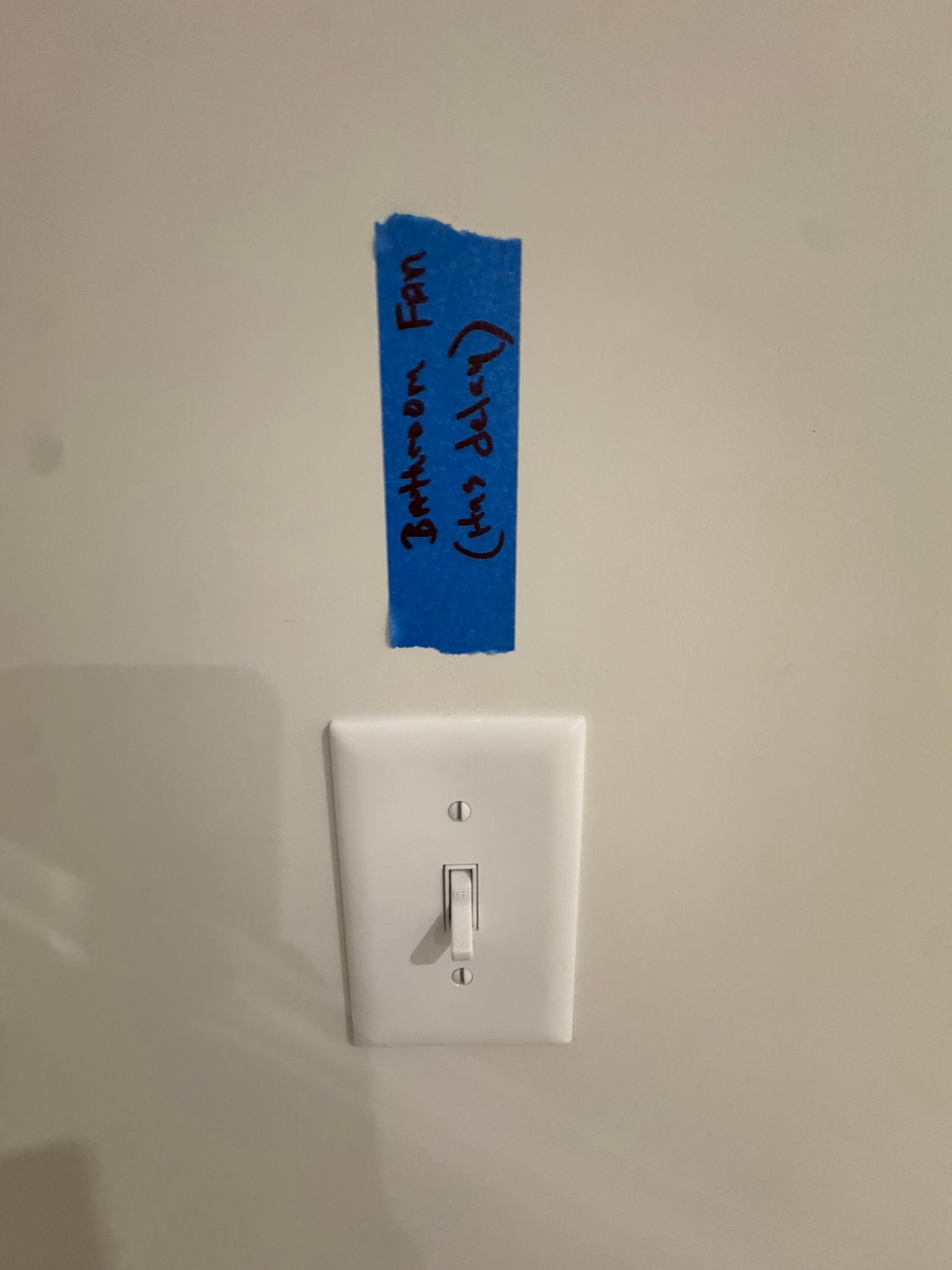 Wall switch beneath blue painter’s tape label on a beige wall