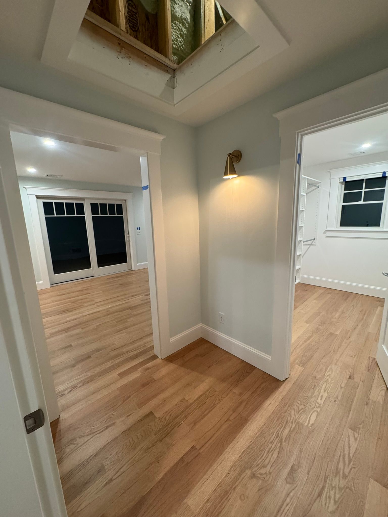 Empty hallway with hardwood floors, white walls, and open doorways to adjoining rooms and a ceiling skylight.