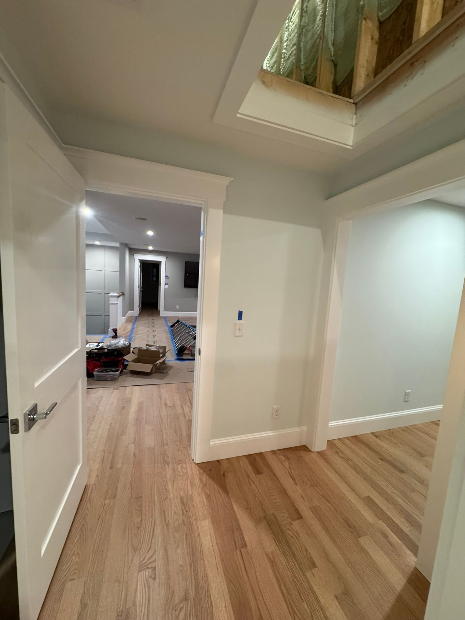Empty white hallway with wood floors, open doorway, and ceiling skylight in a modern home