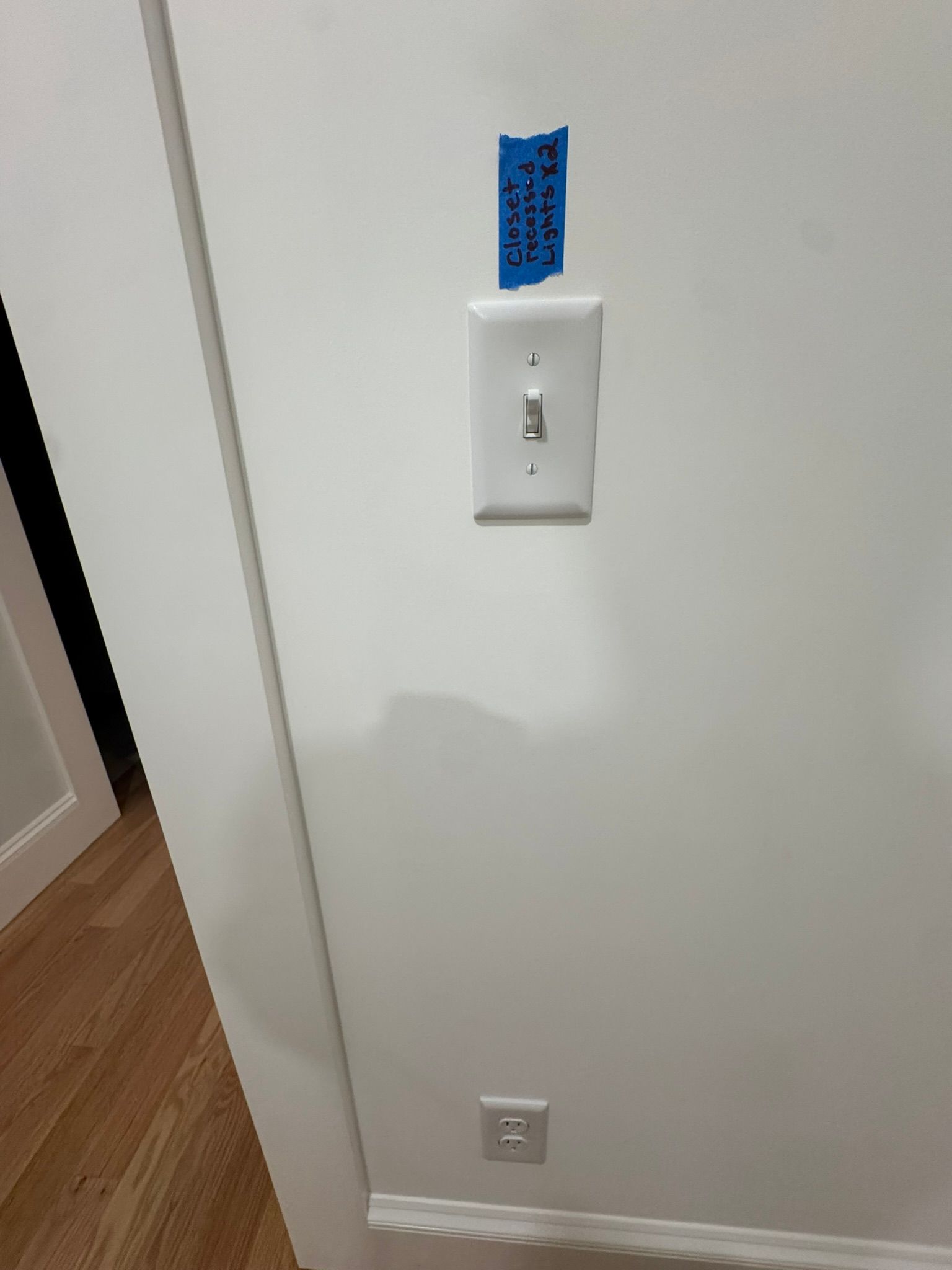 White hallway wall with light switch and outlet, with blue painter’s tape above the switch.