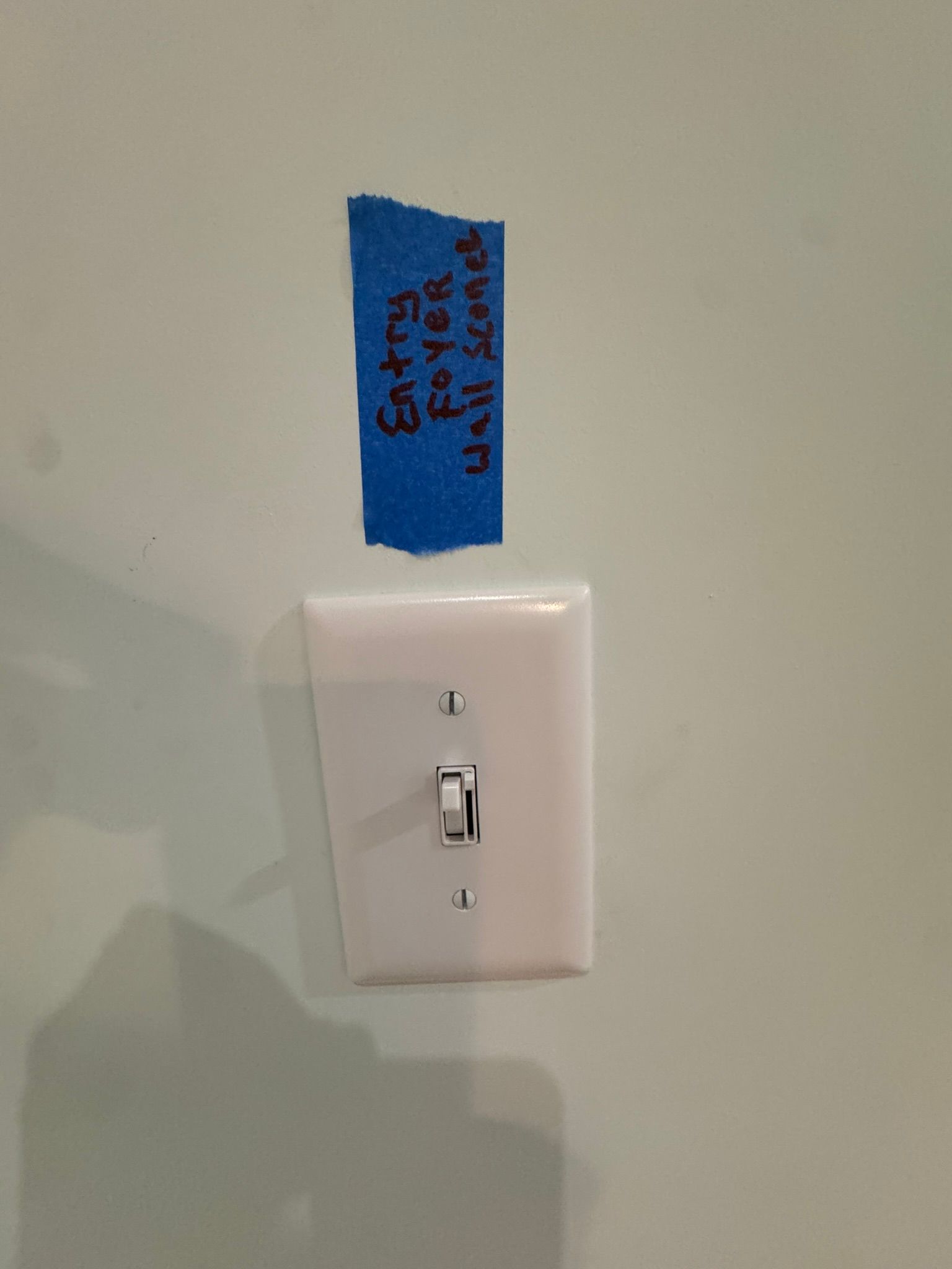 White light switch on a wall with blue tape labeled “Caution” above it.