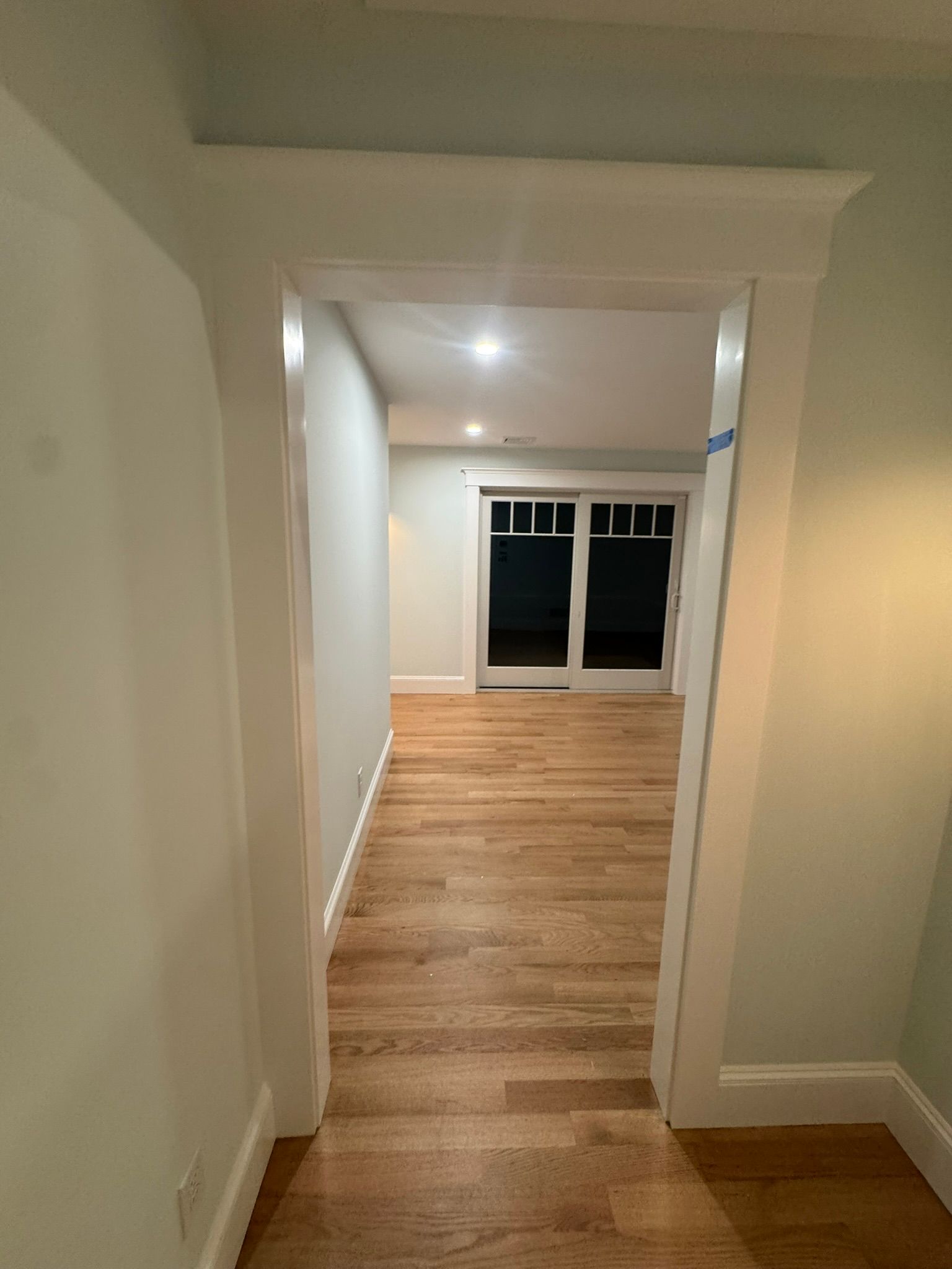 Empty hallway with hardwood floors leading to a bright room with large windows.