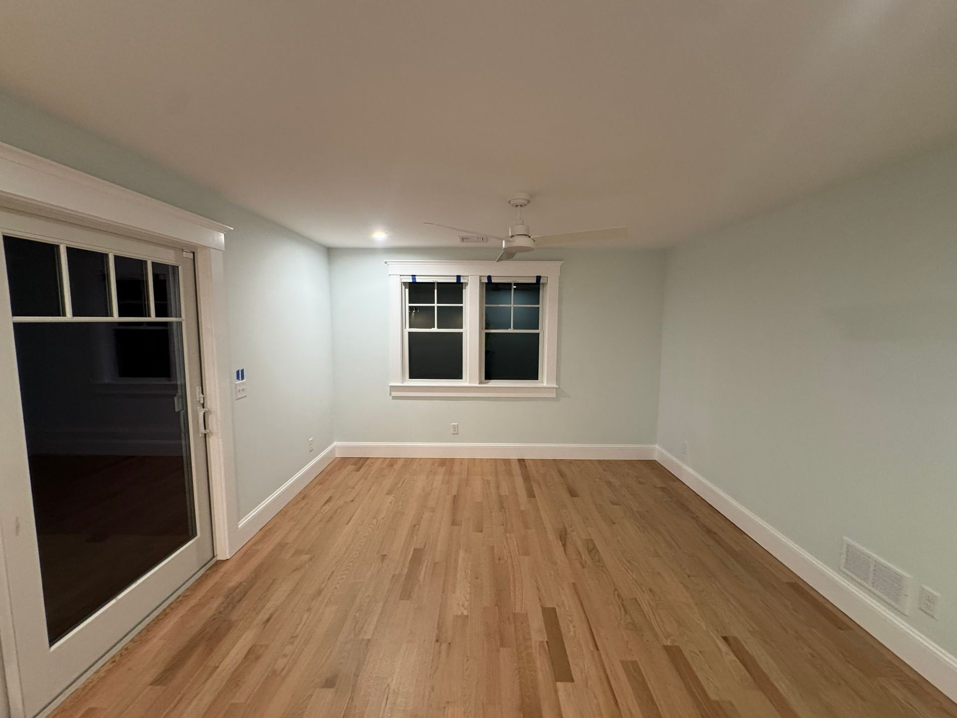 Empty living room with hardwood floors, white walls, and sliding glass door to the left