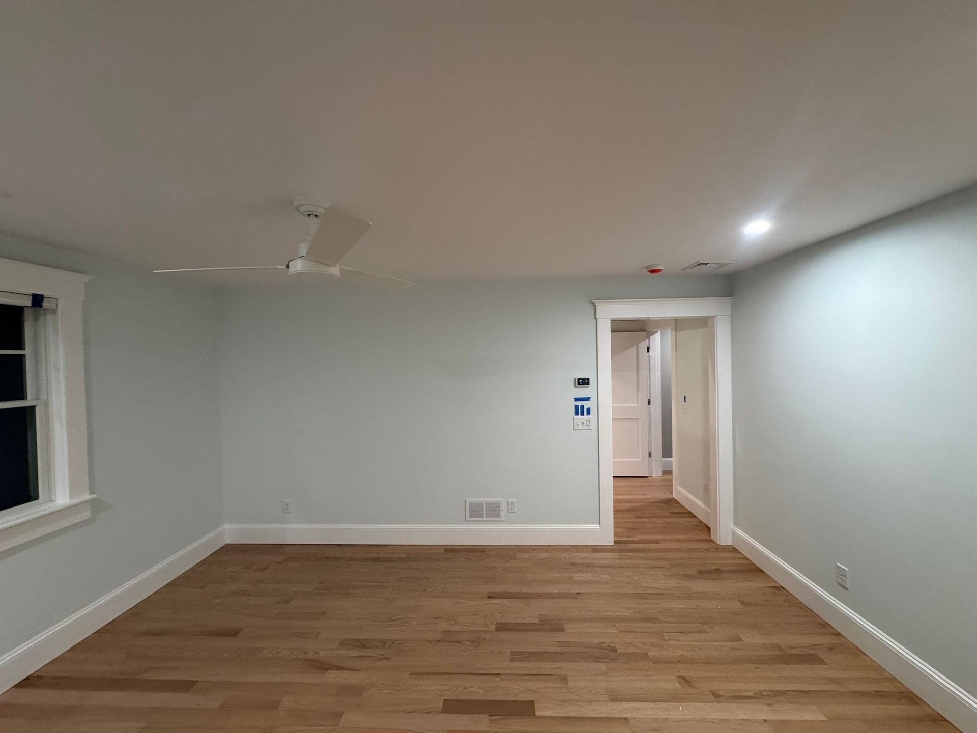 Empty light-blue room with hardwood floors and a doorway to a hallway