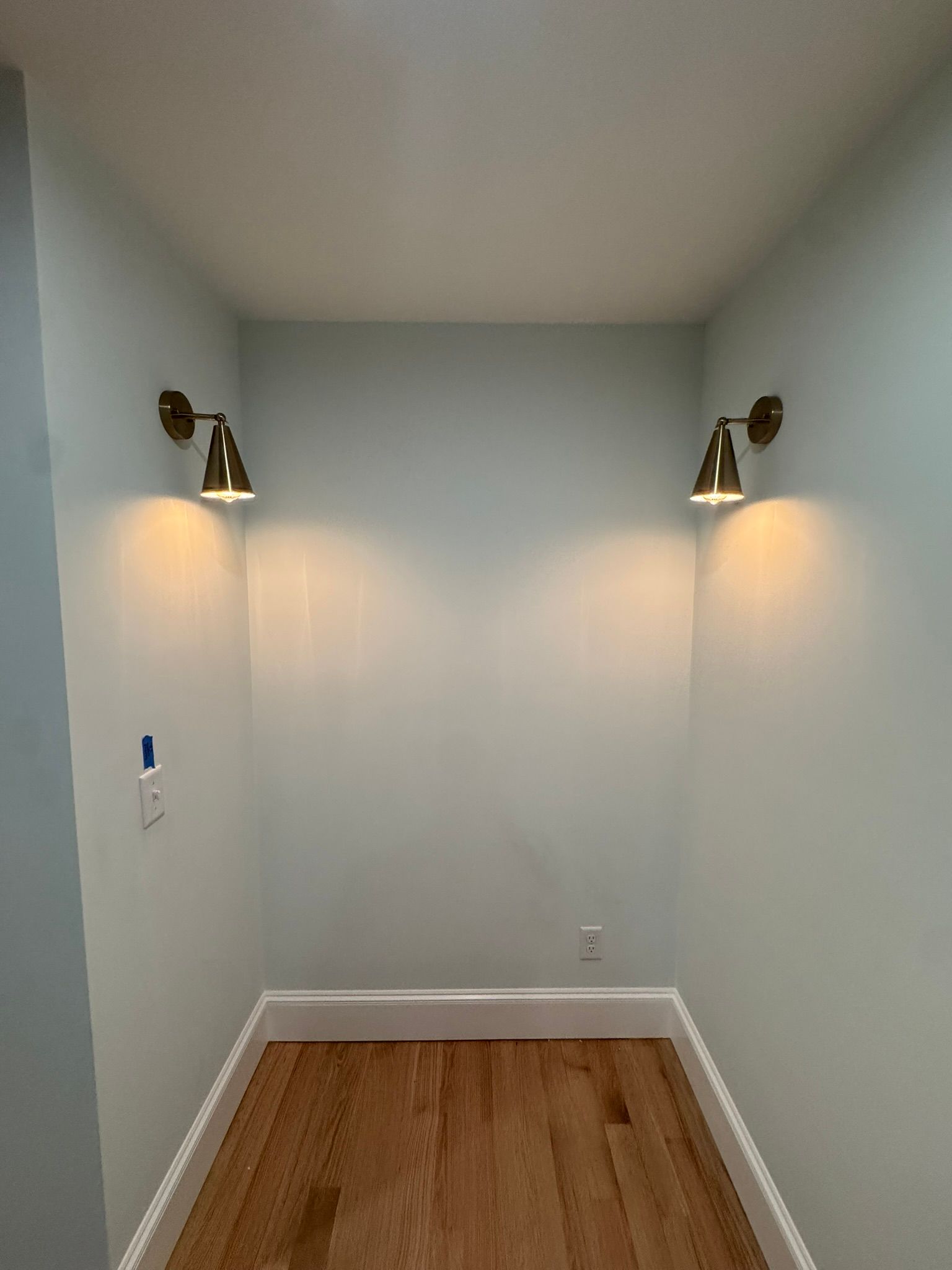Empty narrow room with gray walls, wood floor, and two wall sconces