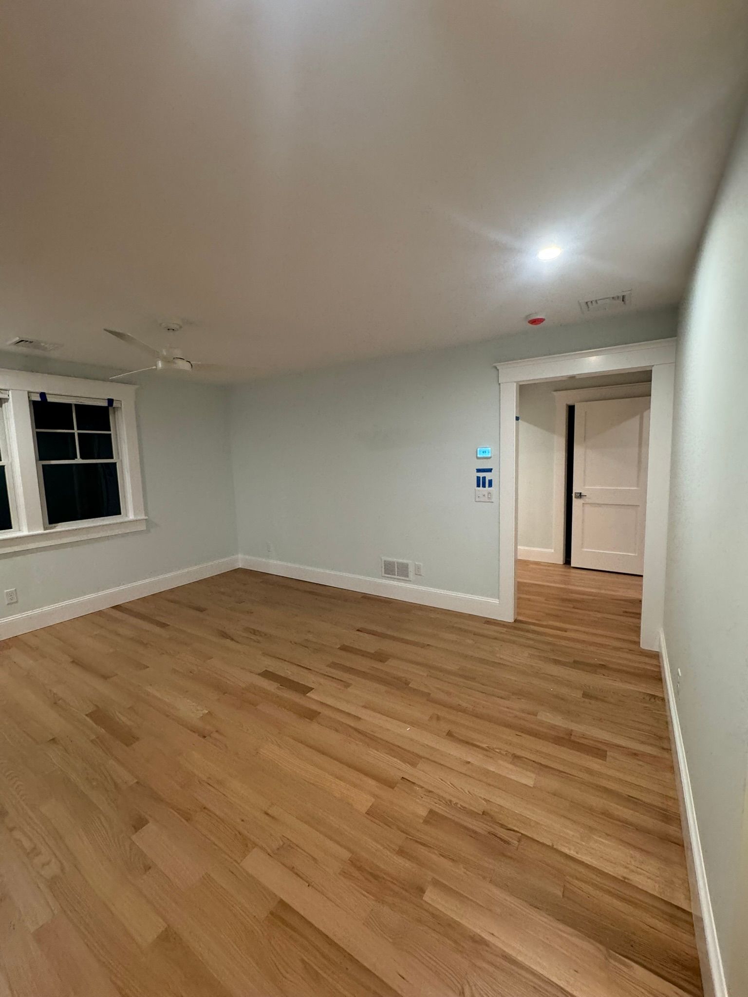 Empty room with light wood floors, white walls, a window, and an open doorway
