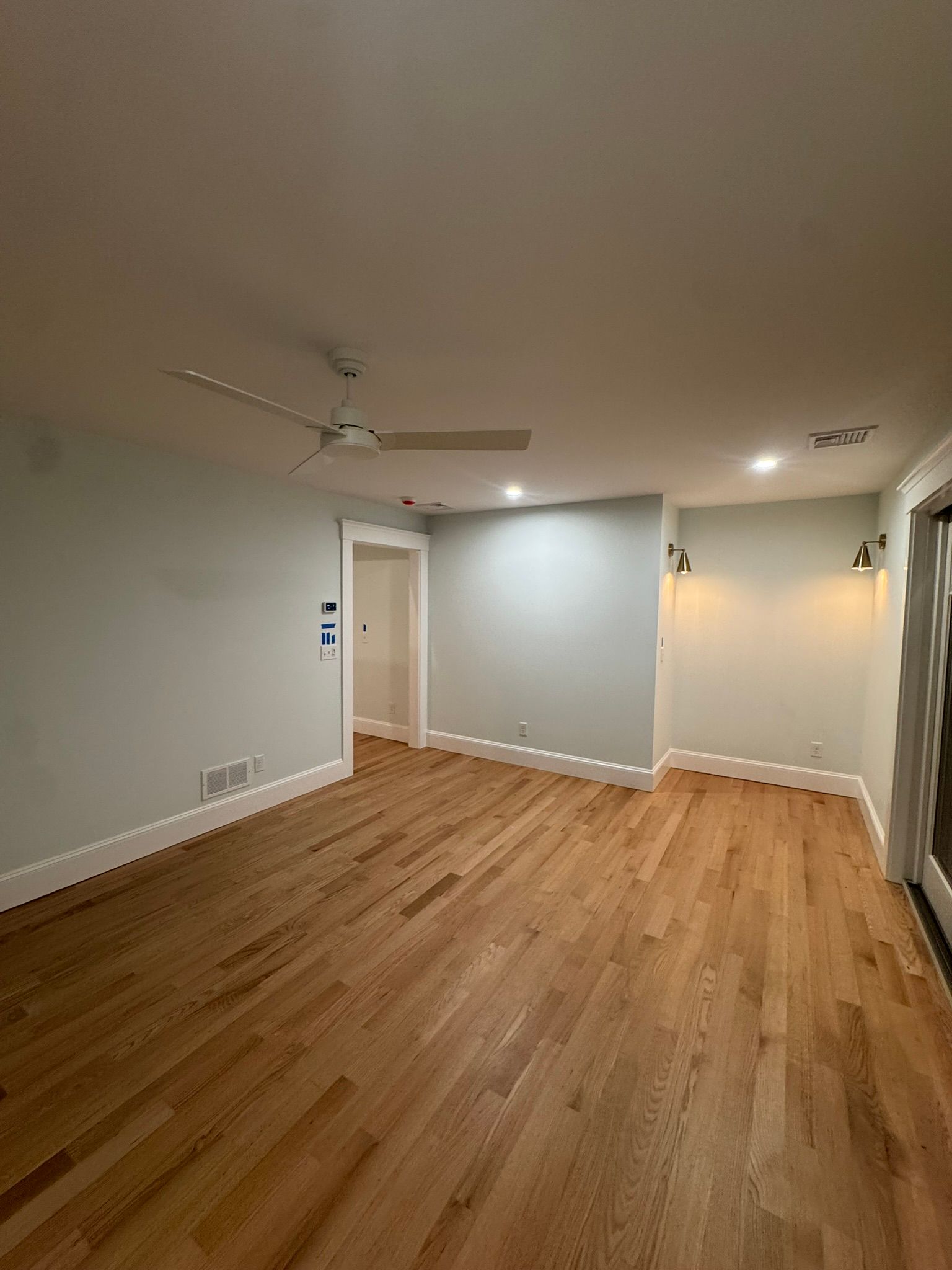 Empty living room with hardwood floors, white walls, ceiling fan, and recessed lighting