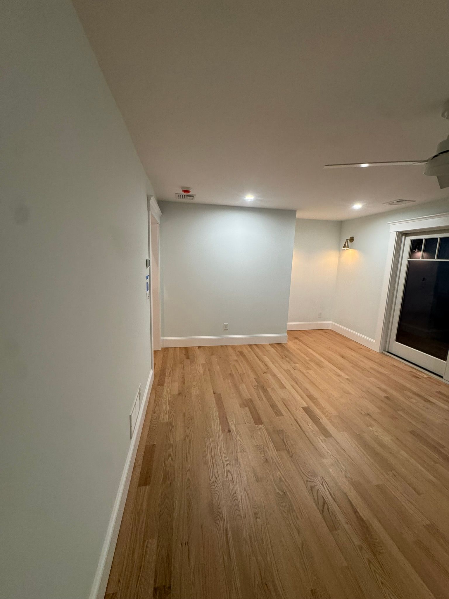 Empty room with light wood flooring, white walls, recessed lights, and a glass door on the right.