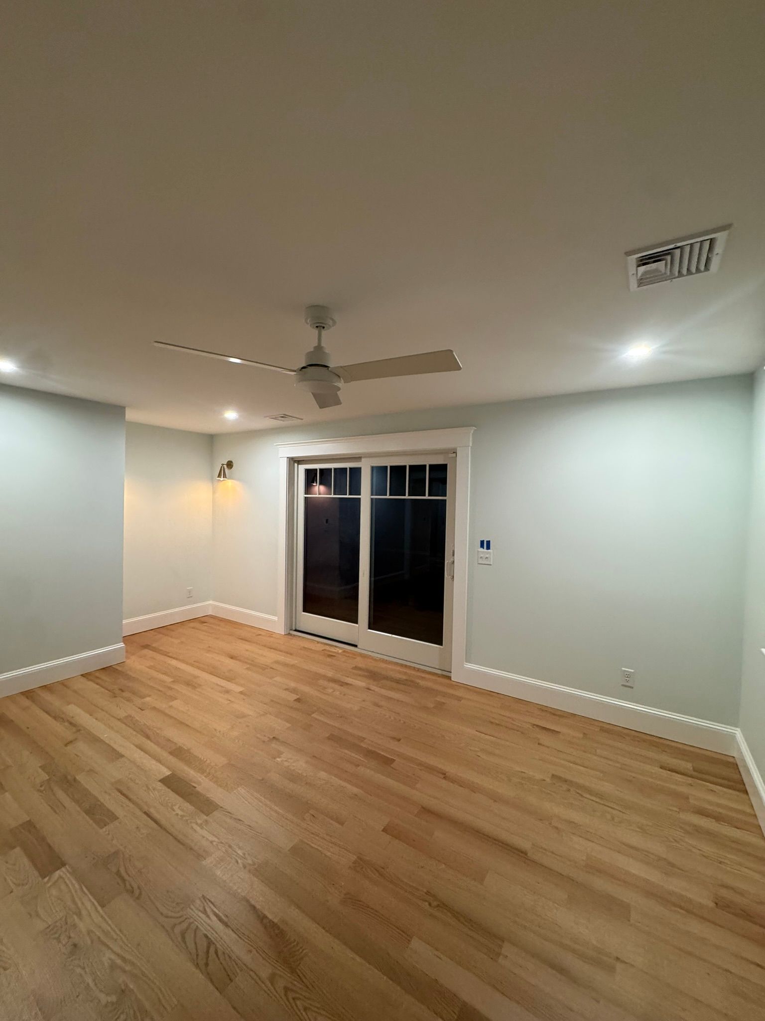 Empty room with hardwood floor, white walls, ceiling fan, and French doors leading outside.