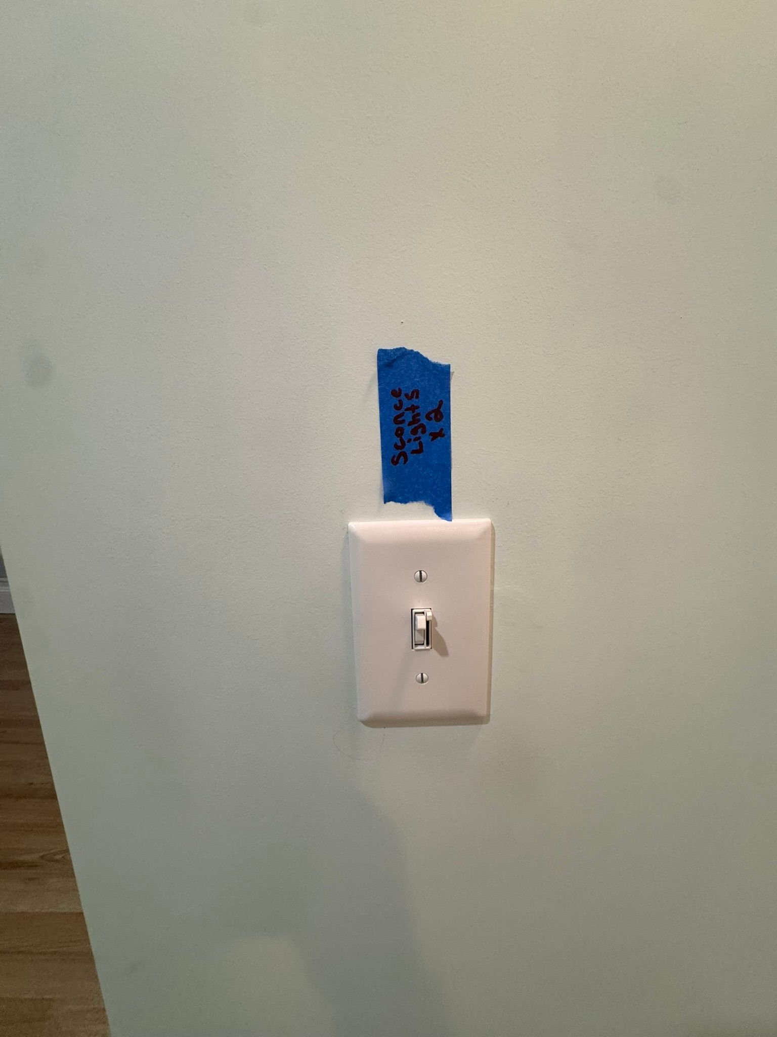 Light switch with blue tape label on a pale green wall