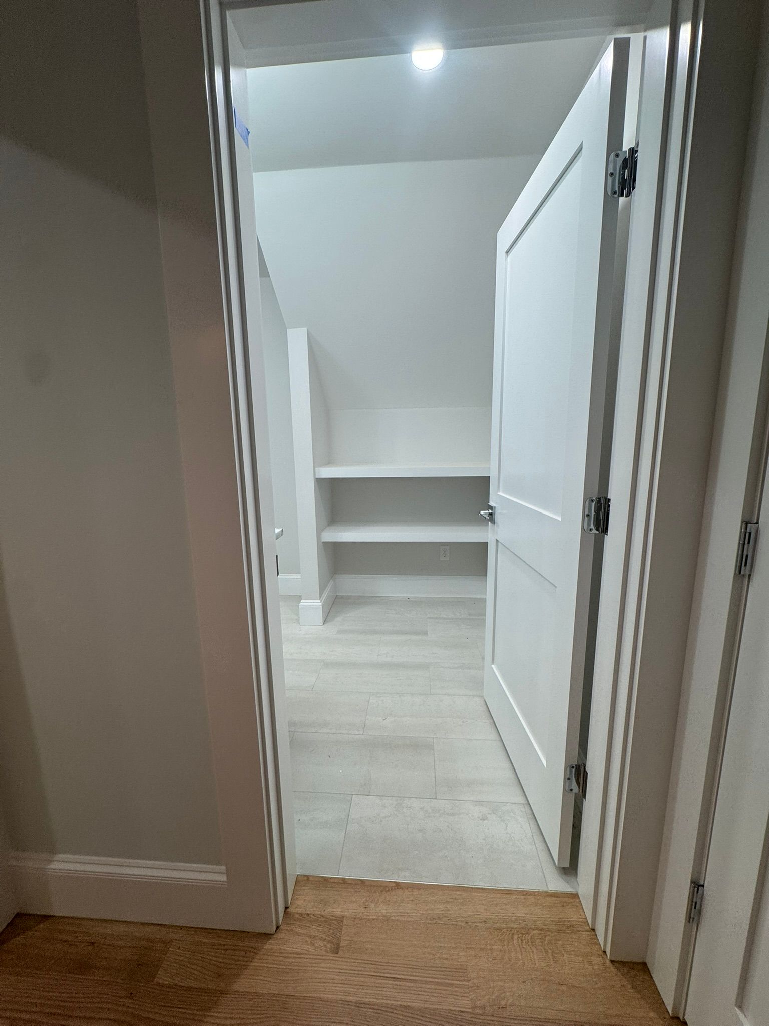 Hallway view into a small empty closet or pantry with white shelves and an open door