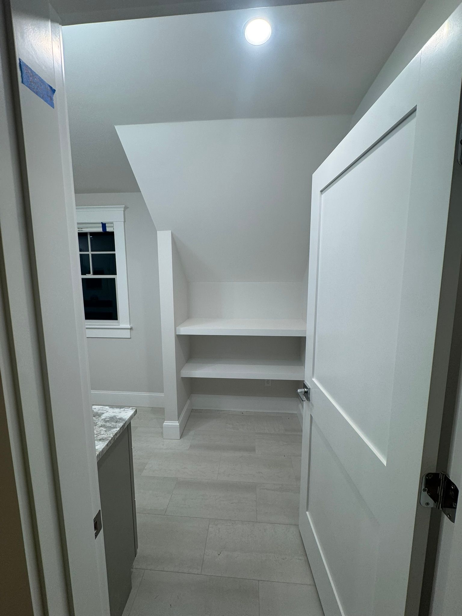 Narrow white hallway with sloped ceiling, built-in shelves, and closed closet doors.