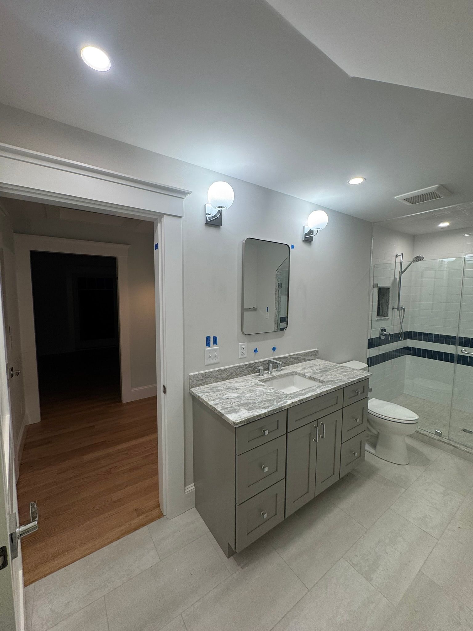 Bright bathroom with double vanity, mirror lights, tiled floor, and glass shower.