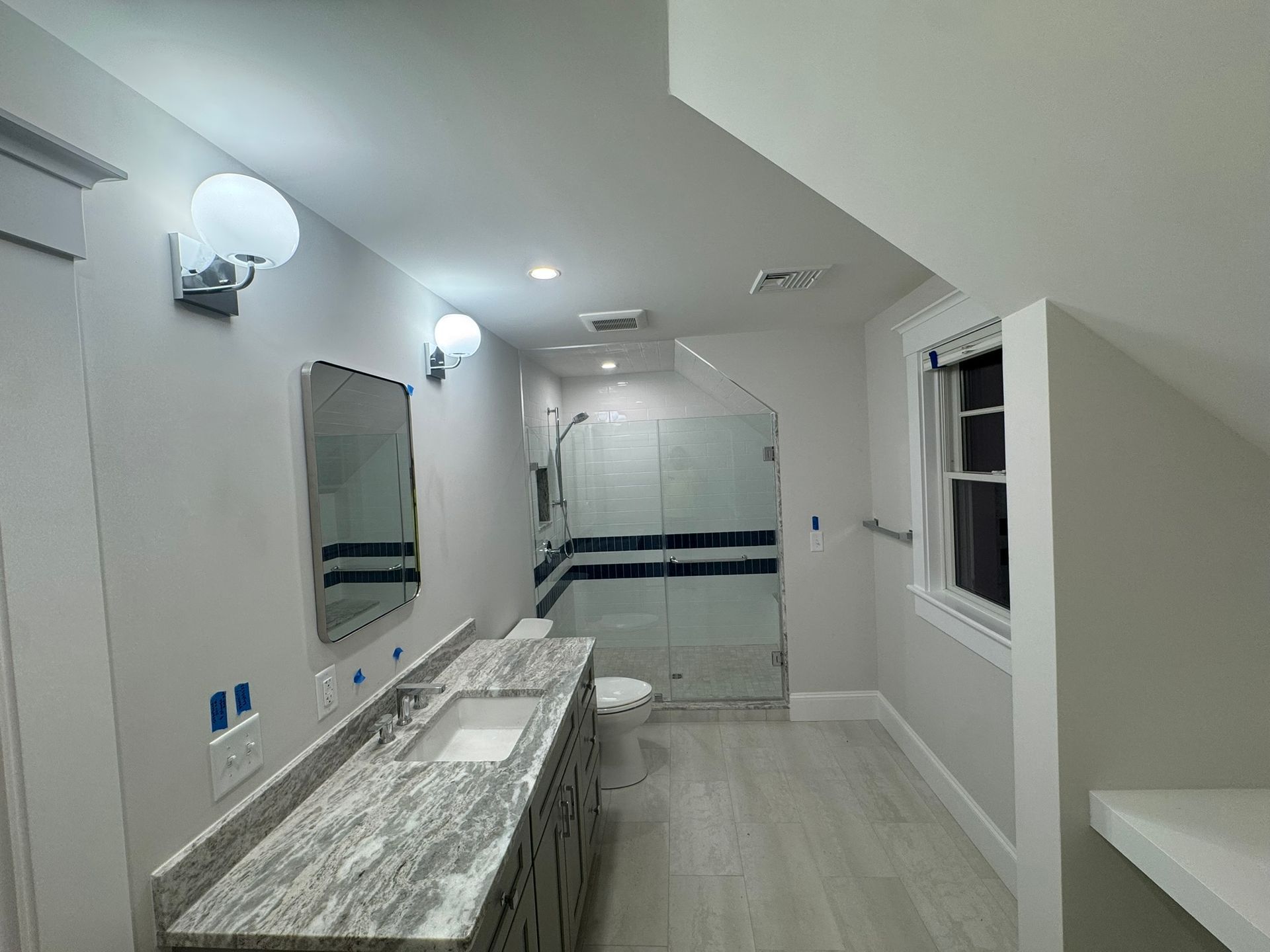 Modern bathroom with double vanity, large mirror, glass shower, and white walls and tile.