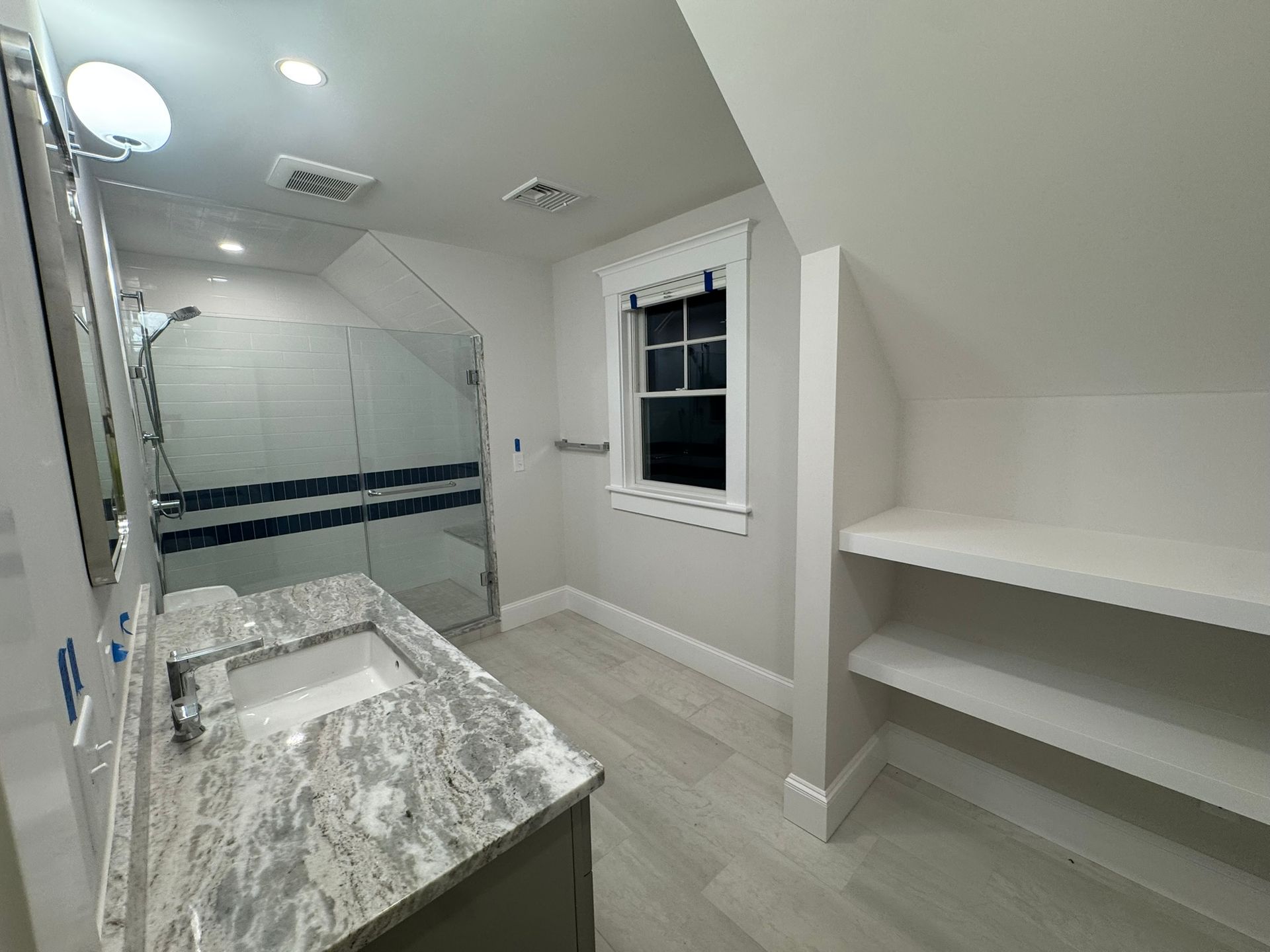 Bright bathroom with marble vanity, glass shower, window, and white shelves