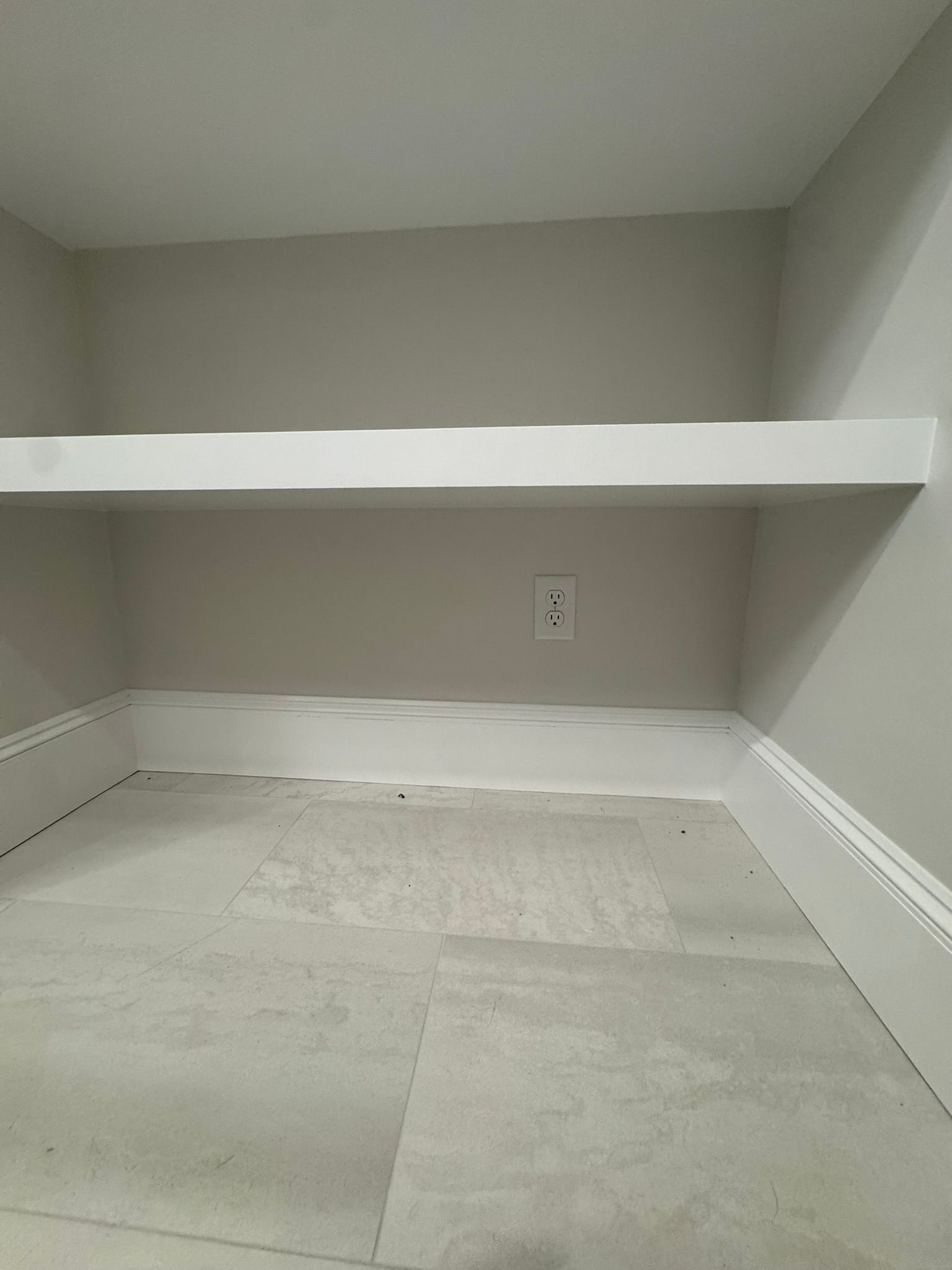 Empty gray closet with built-in shelf and white tile floor