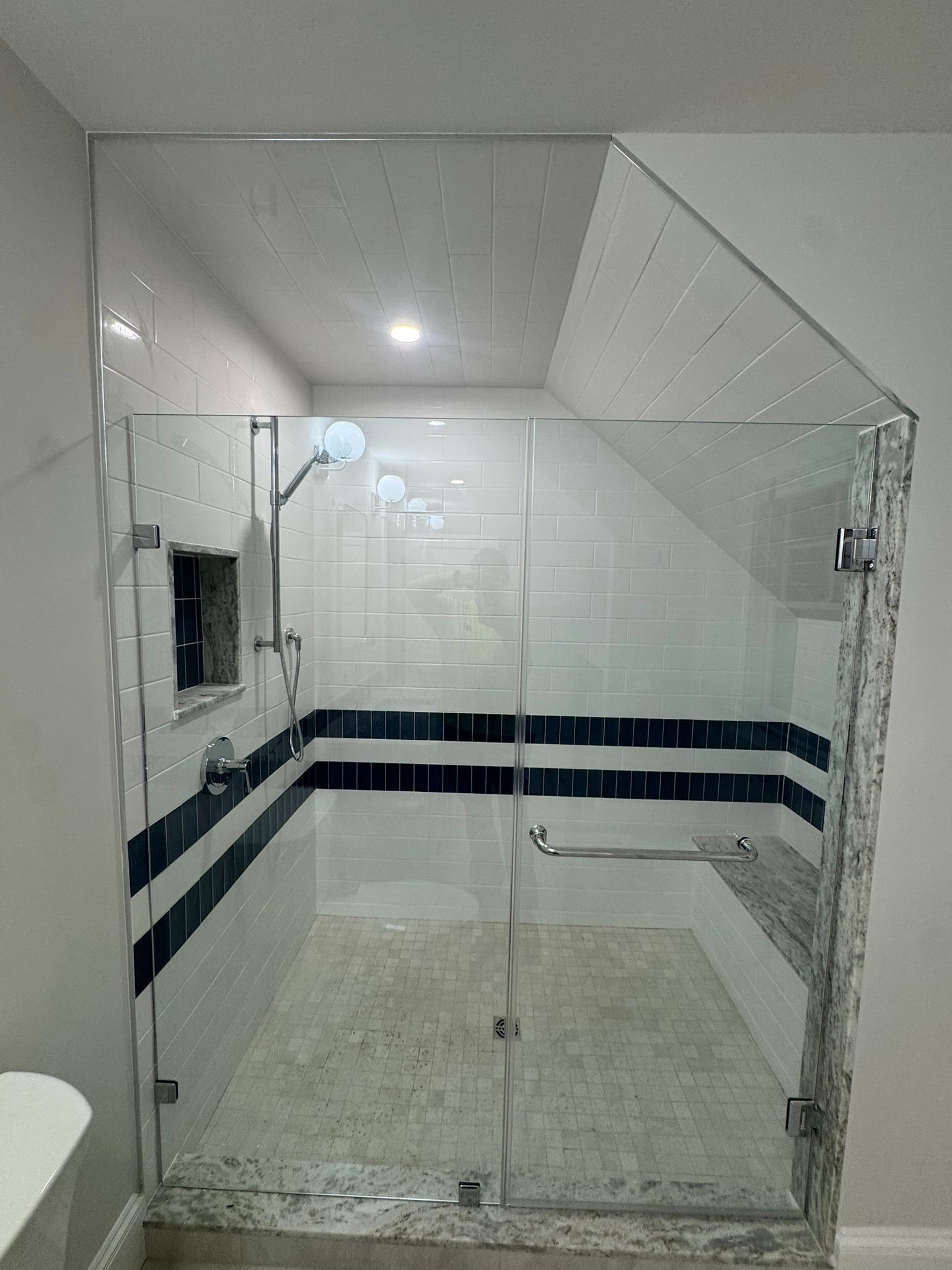 Glass-walled shower with white tile, navy stripe, and chrome grab bars in a bathroom