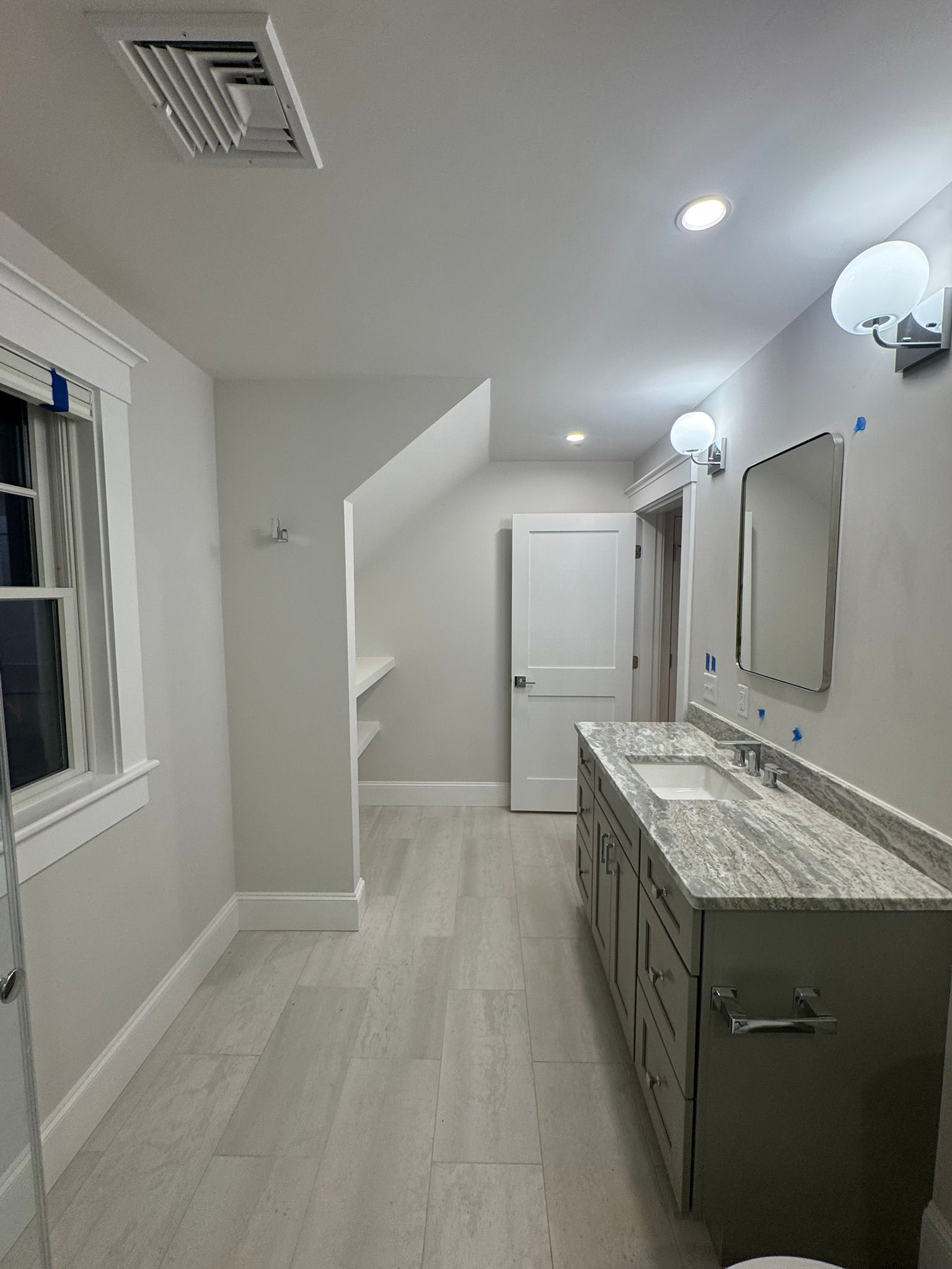 Bright bathroom with a double vanity, mirrors, white walls, and a doorway in the back.
