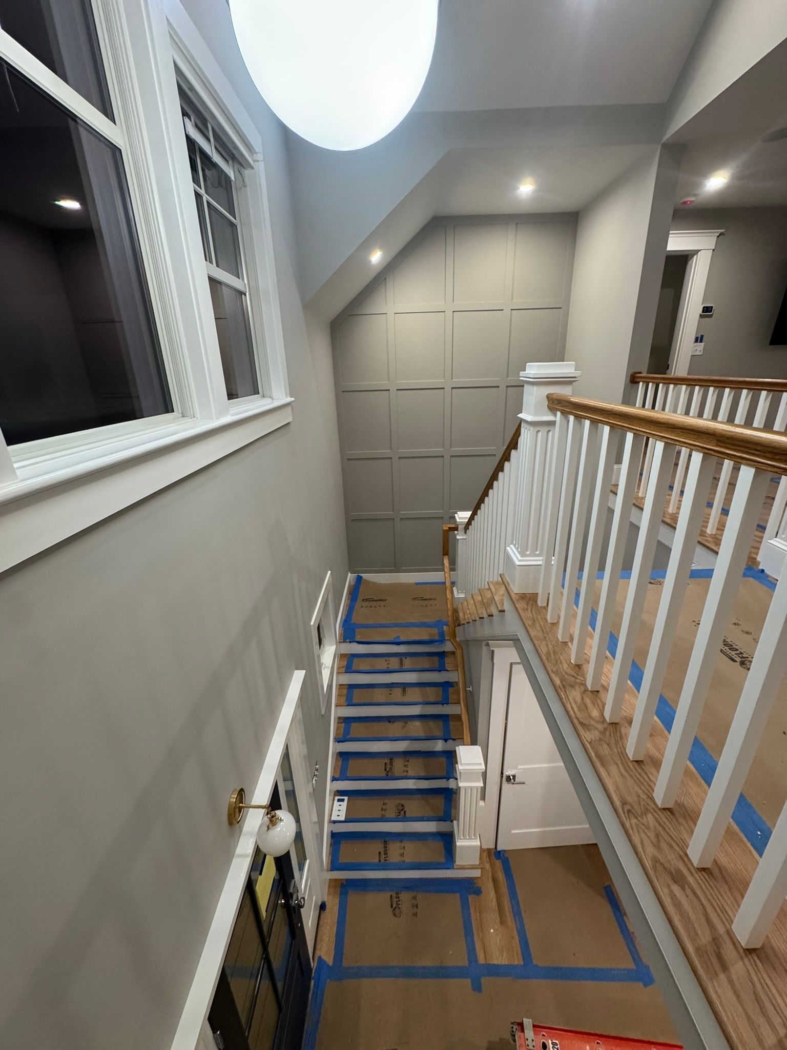 Indoor staircase under construction, with blue tape on steps, white railing, and a hallway landing.