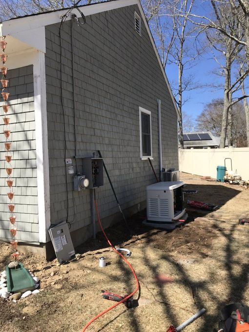 Side of a house with an outdoor HVAC unit, utility meter, and extension cord in a yard.