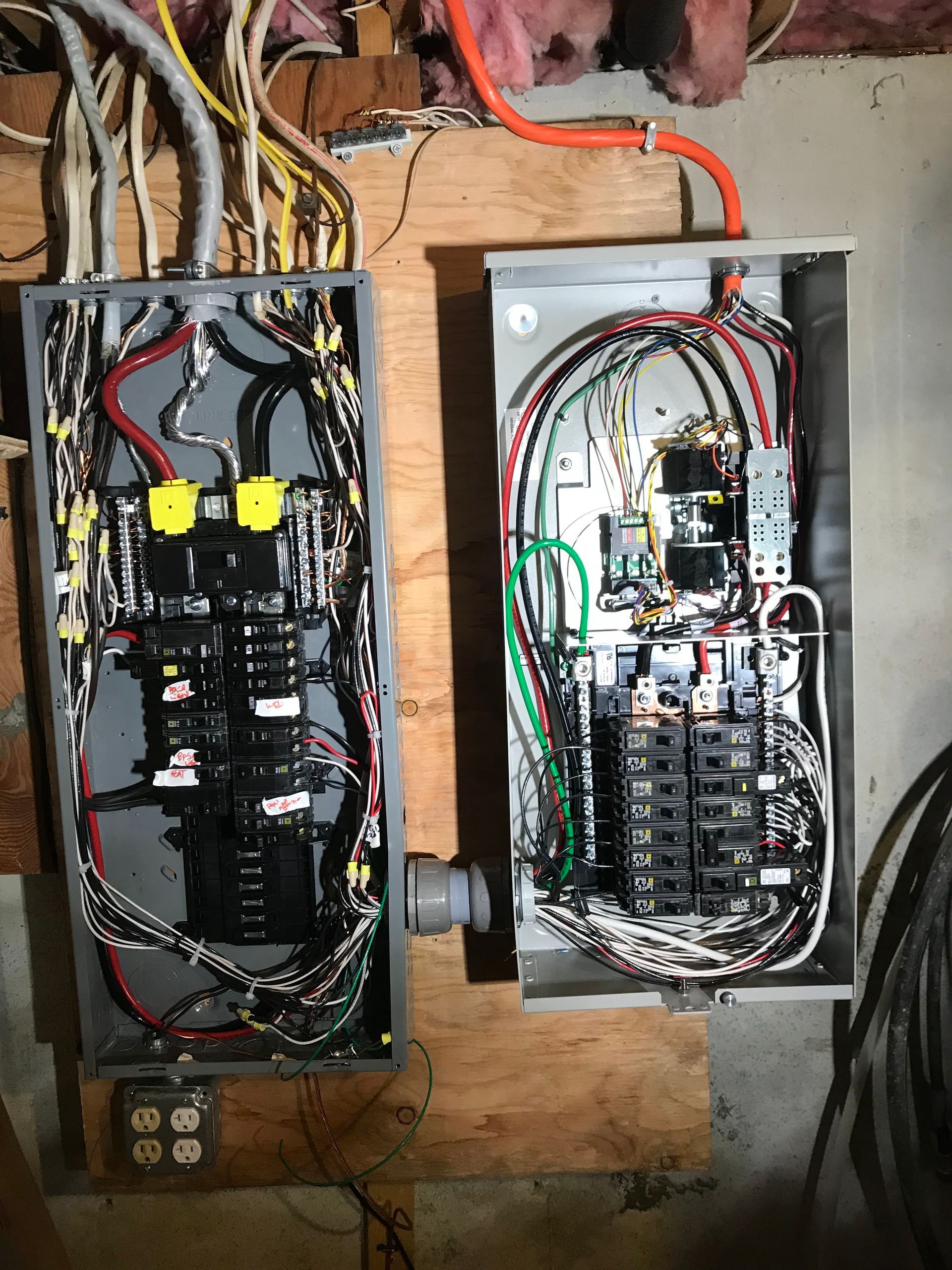 Two open electrical breaker panels with exposed wiring mounted on a plywood wall.