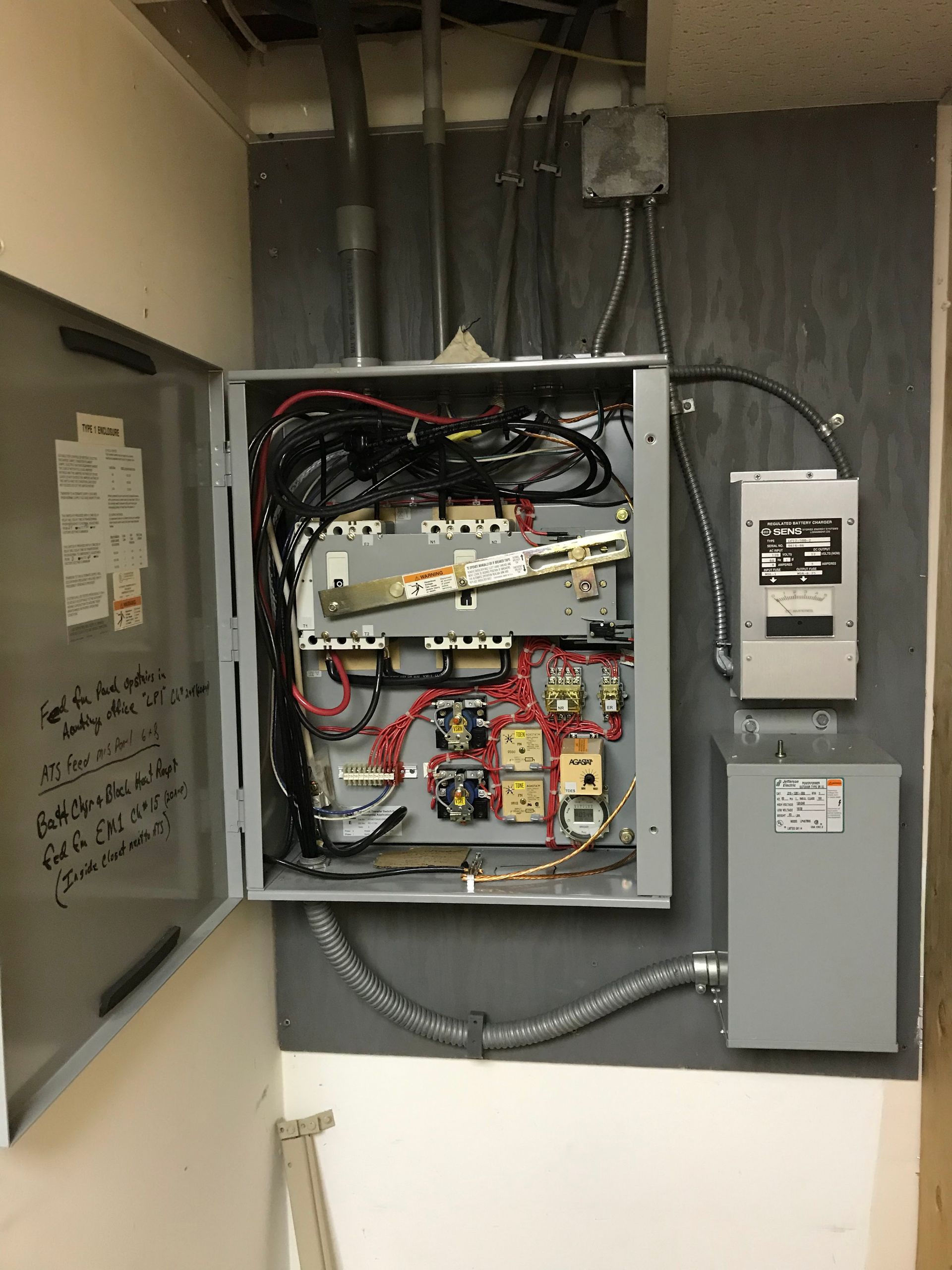 Open electrical control panel with wiring, breakers, and gray conduit in a utility room