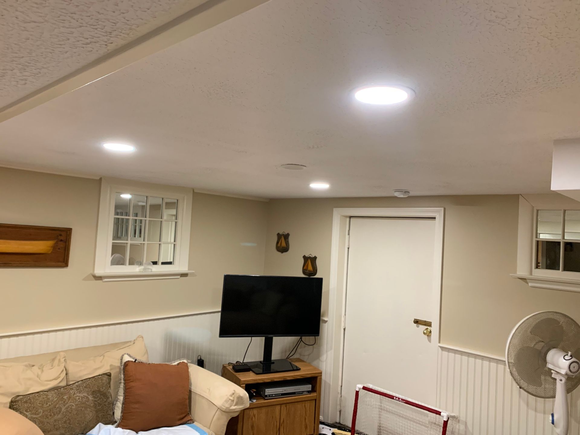 Basement living room with couch, TV, fan, and white door under recessed ceiling lights