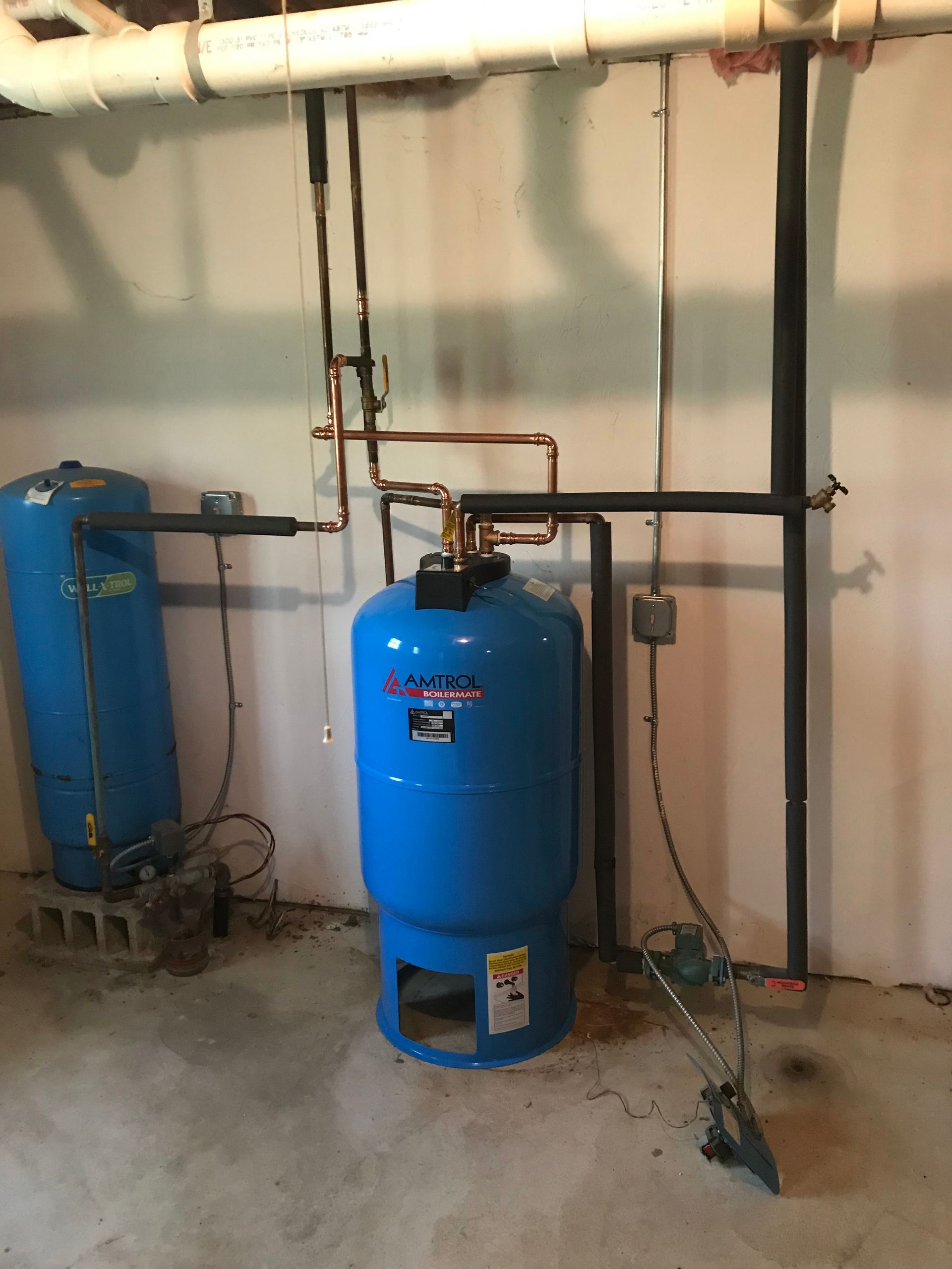 Two blue industrial tanks with copper piping and valves in a utility room