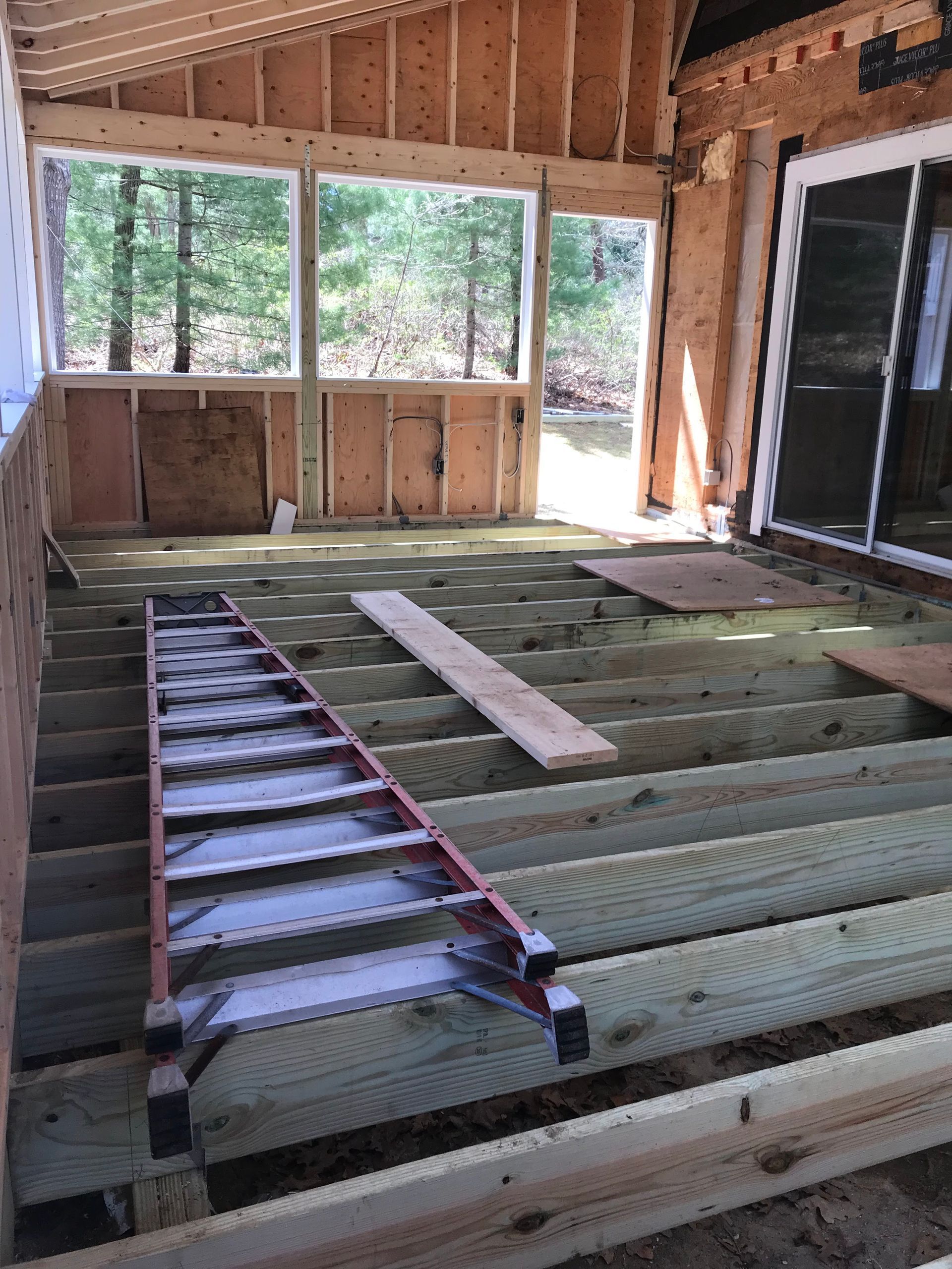 Unfinished room floor with exposed joists, ladder, and insulation boards in a wooden-framed house