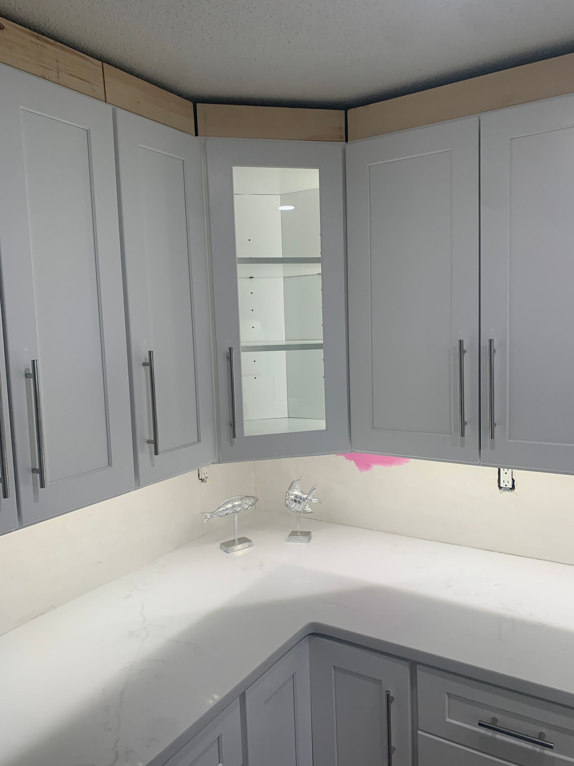 Gray kitchen cabinets with a white countertop and sink in a corner layout