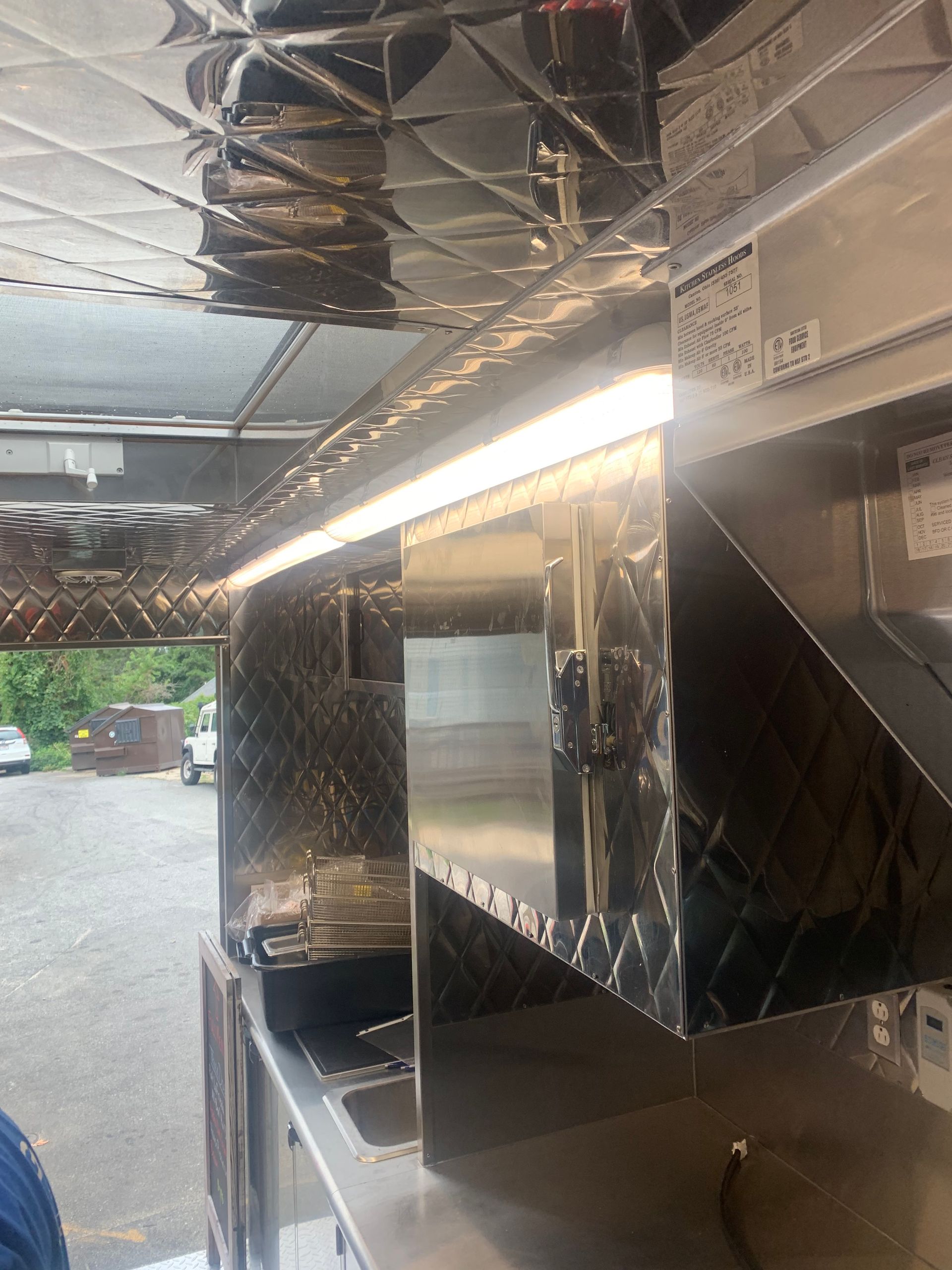 Stainless steel kitchen vent hood and backsplash under bright overhead lights in a narrow food prep area