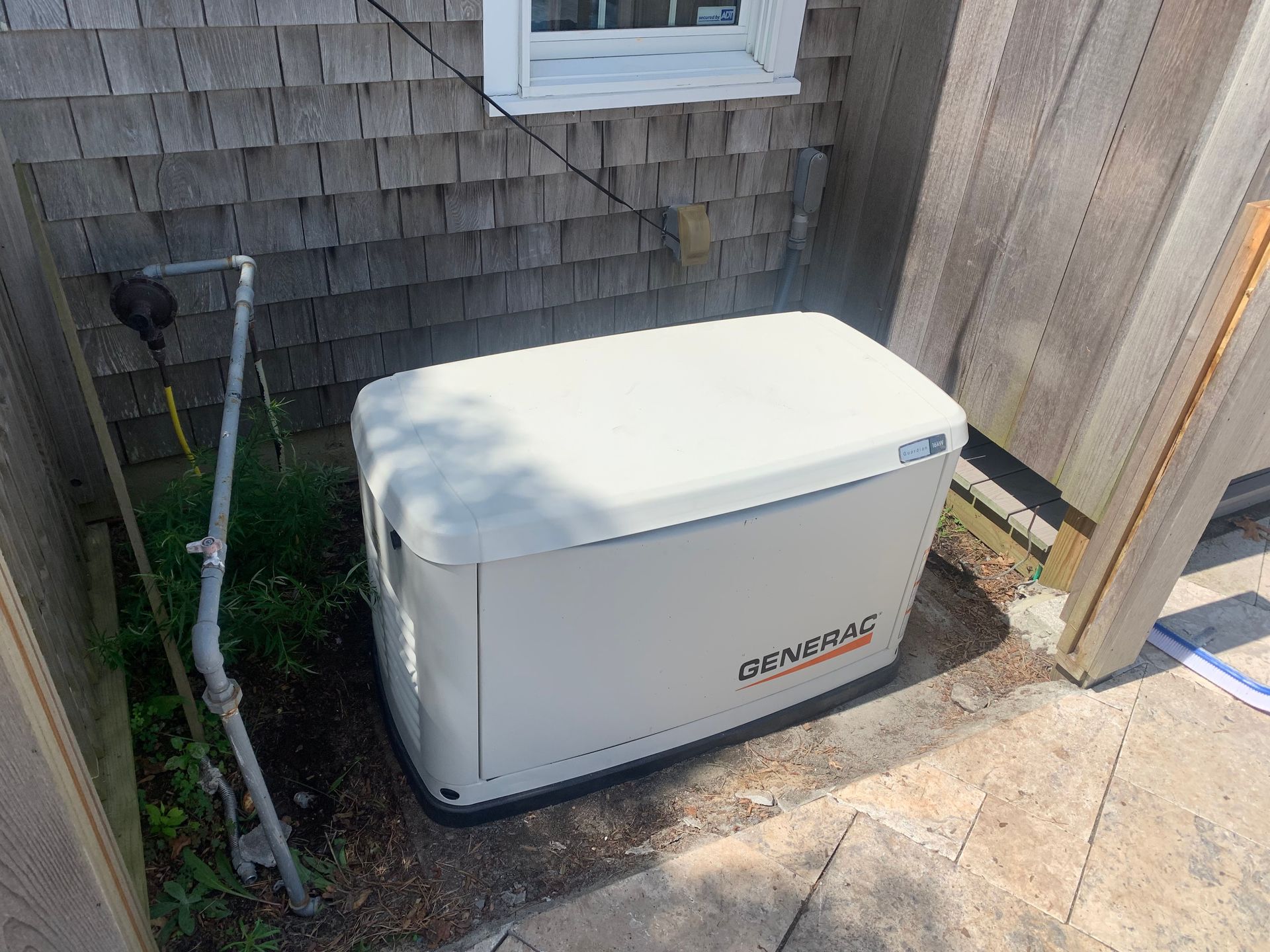 White Generac generator beside a house and fence on a concrete pad outdoors
