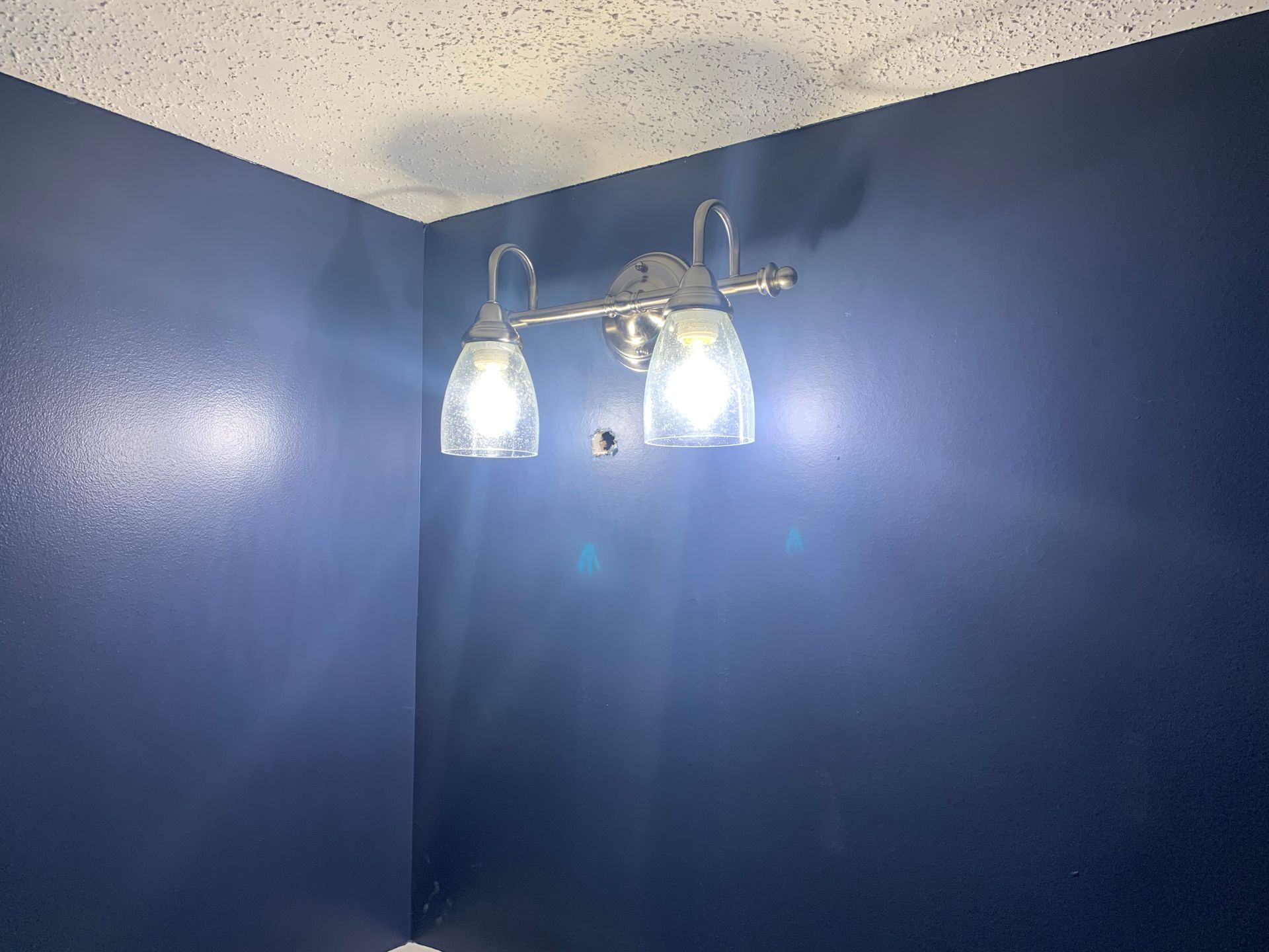 Blue bathroom corner with a two-light wall sconce and textured ceiling