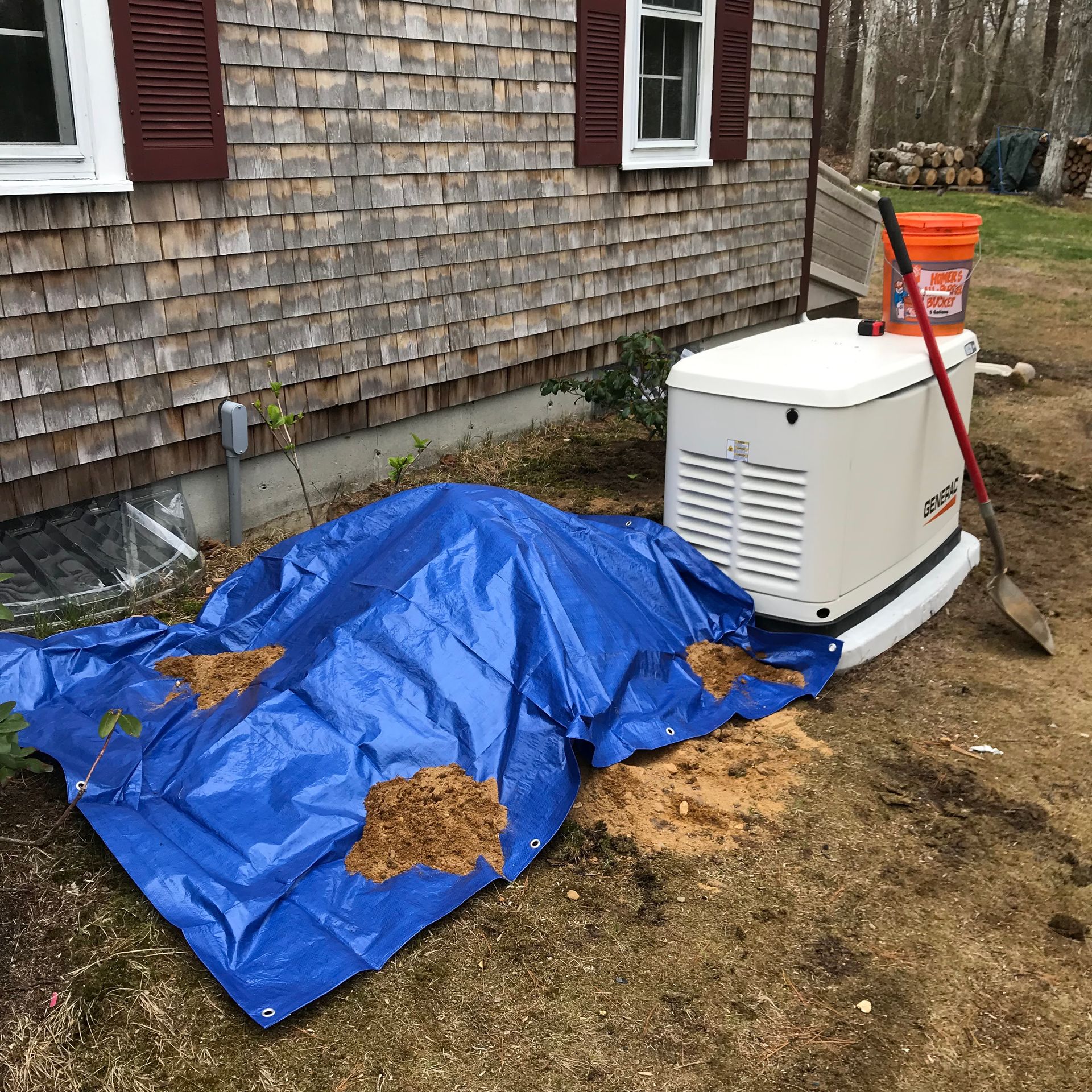 Blue tarp covering debris beside a house, next to a white generator in a muddy yard.