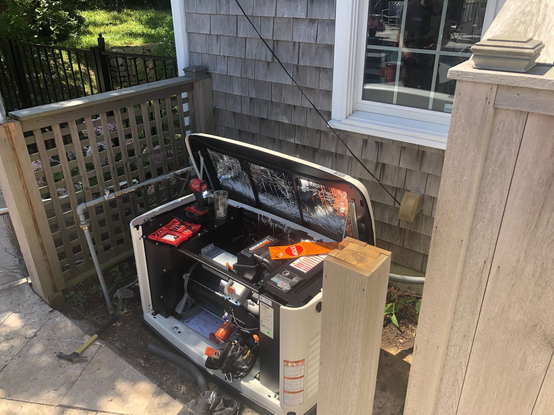 Portable generator on a wooden deck beside a house, with its top open and a cardboard box nearby.