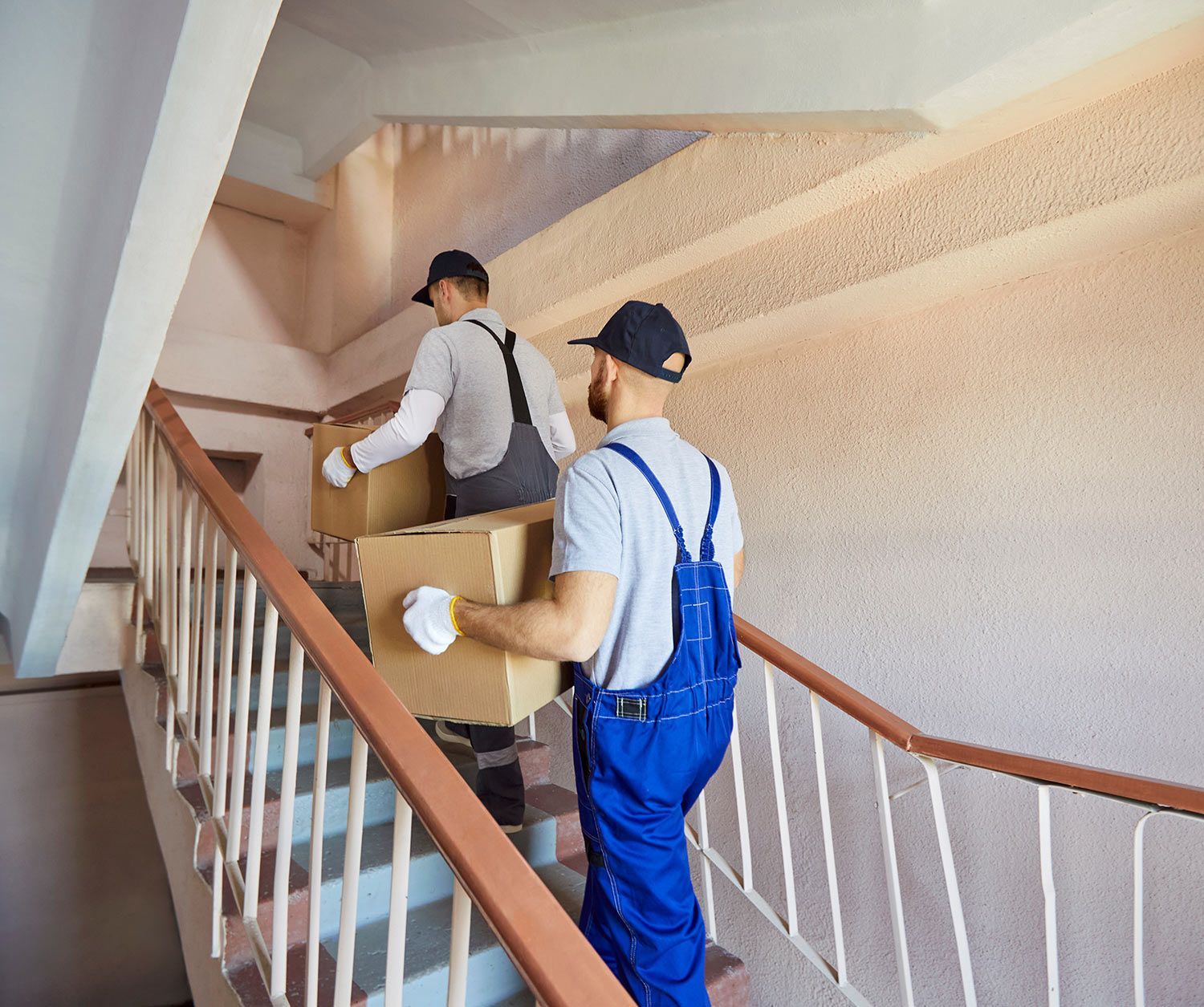 Two workers carrying boxes up an indoor stairwell