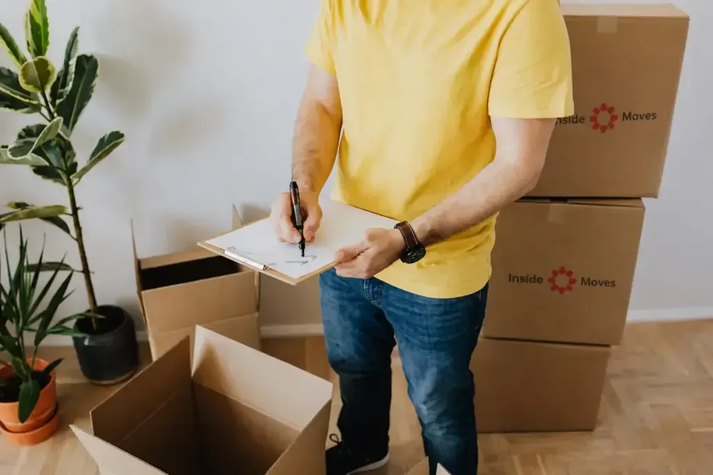 Person writing on a notepad beside stacked moving boxes