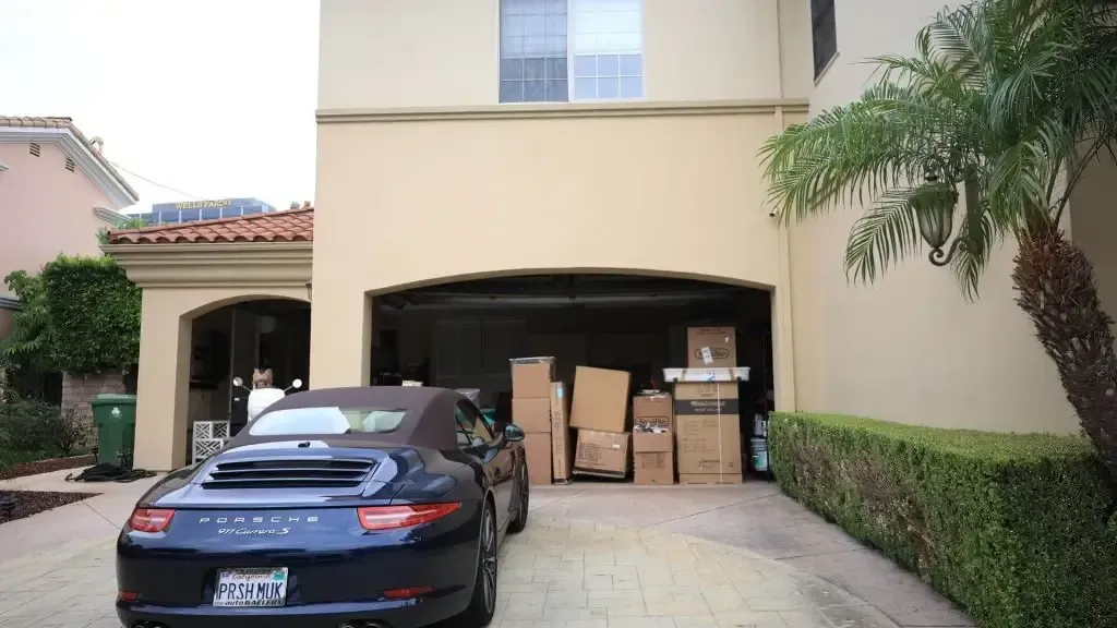 Black car parked in a driveway beside a house with stacked moving boxes