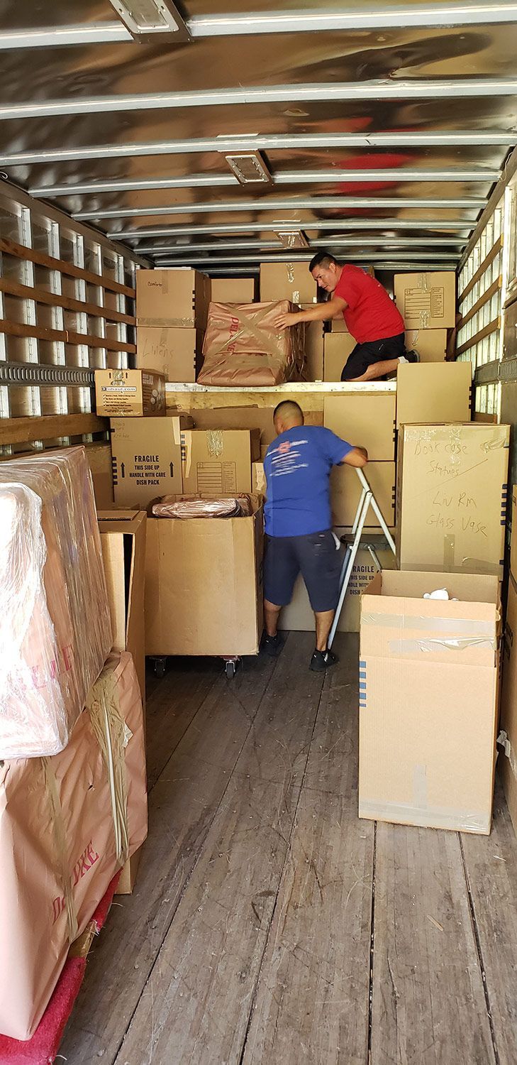 People loading stacked cardboard boxes inside a truck trailer