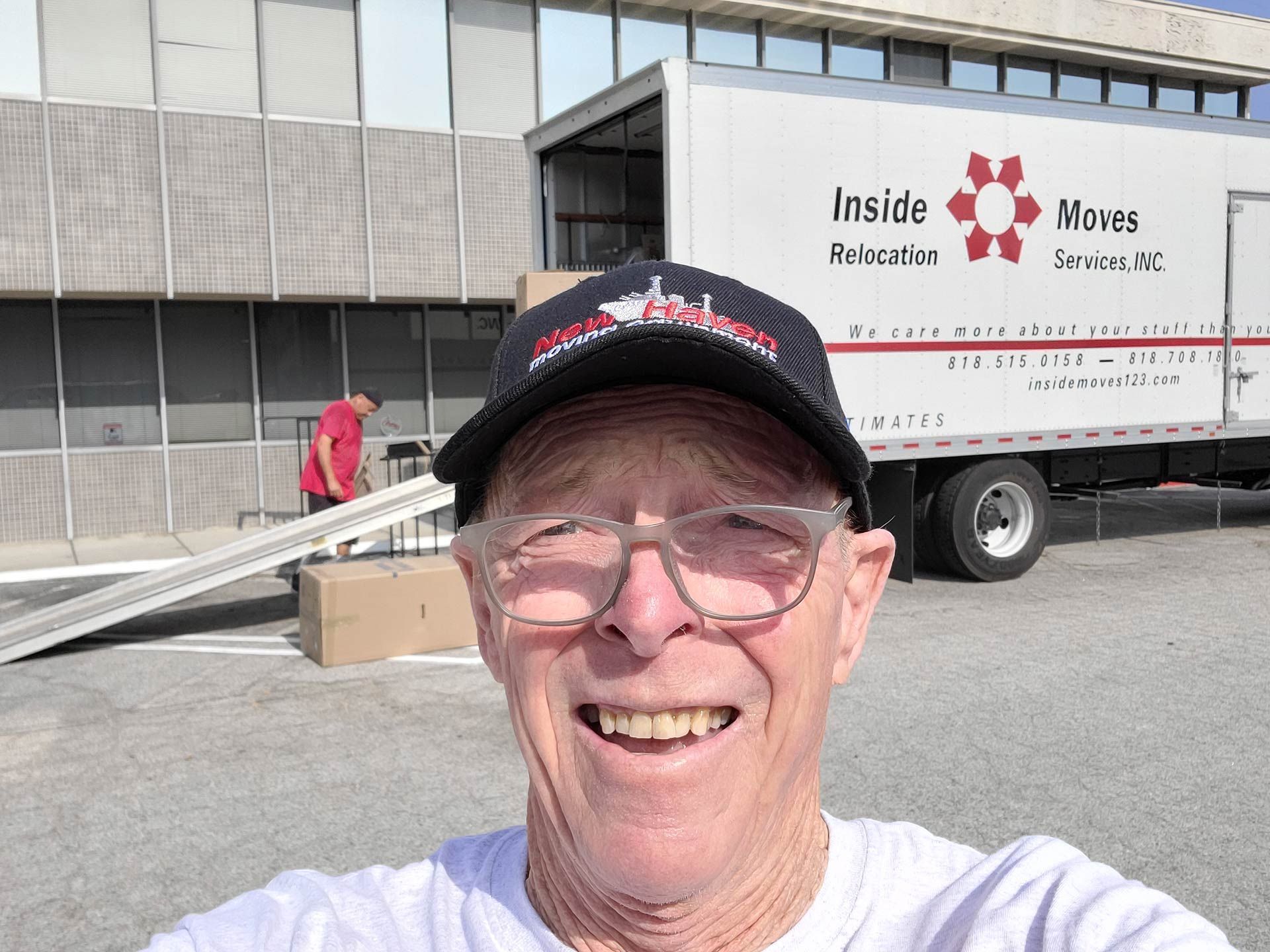 Smiling man in black cap and glasses in front of a moving truck