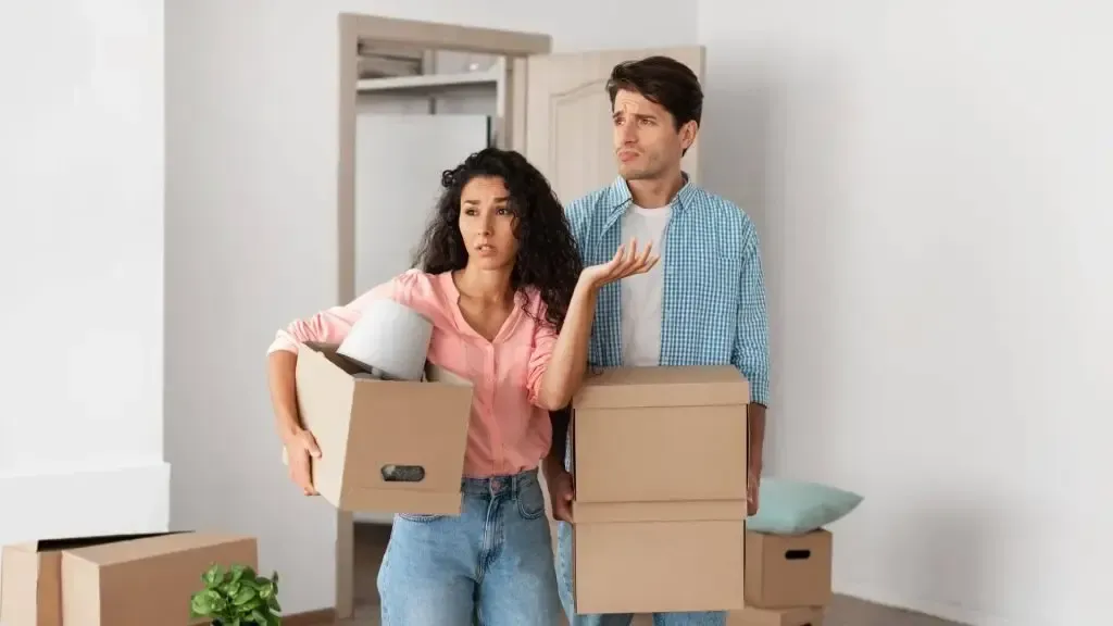 Two people carrying moving boxes in a doorway