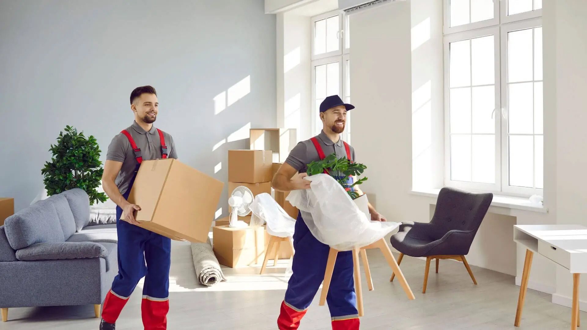 Two movers carry boxes through a bright living room