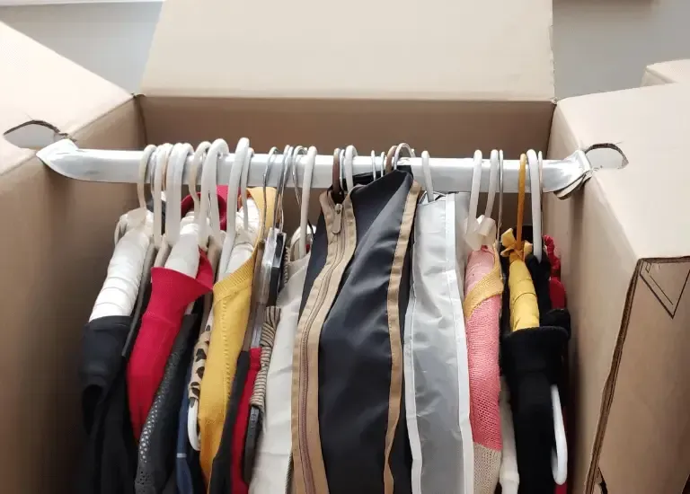 Clothing hanging on hangers inside an open moving box