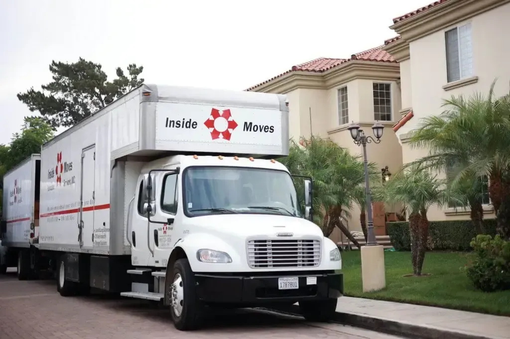 White moving truck parked on a driveway beside a large house