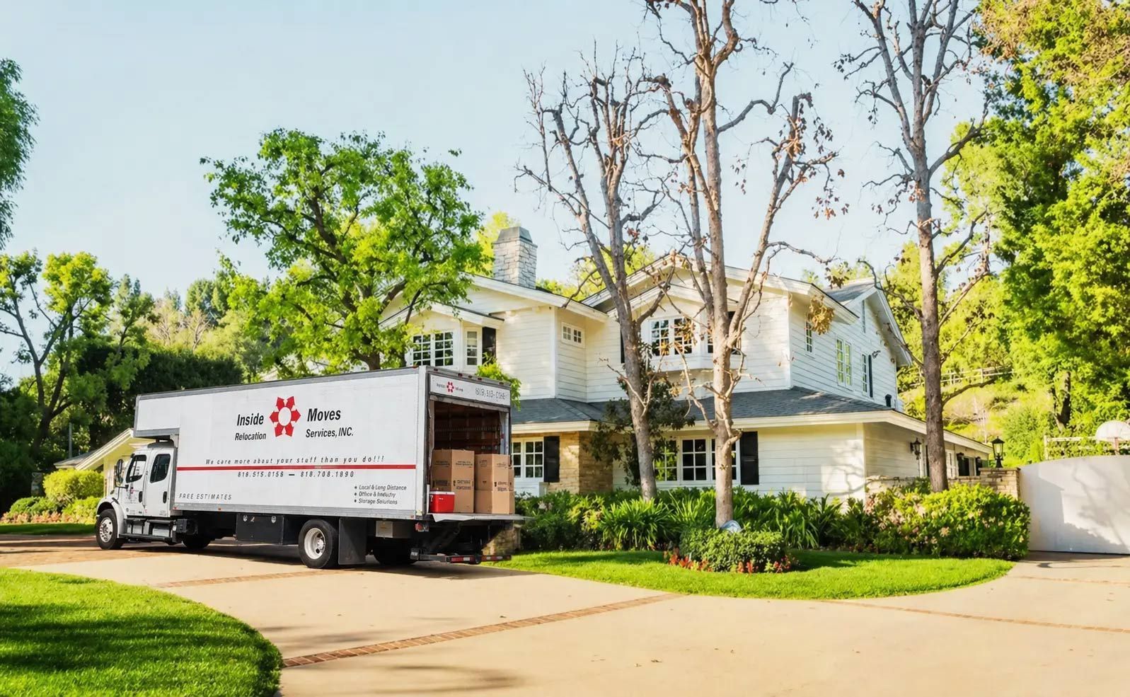 Moving truck parked outside a white house with trees and a driveway