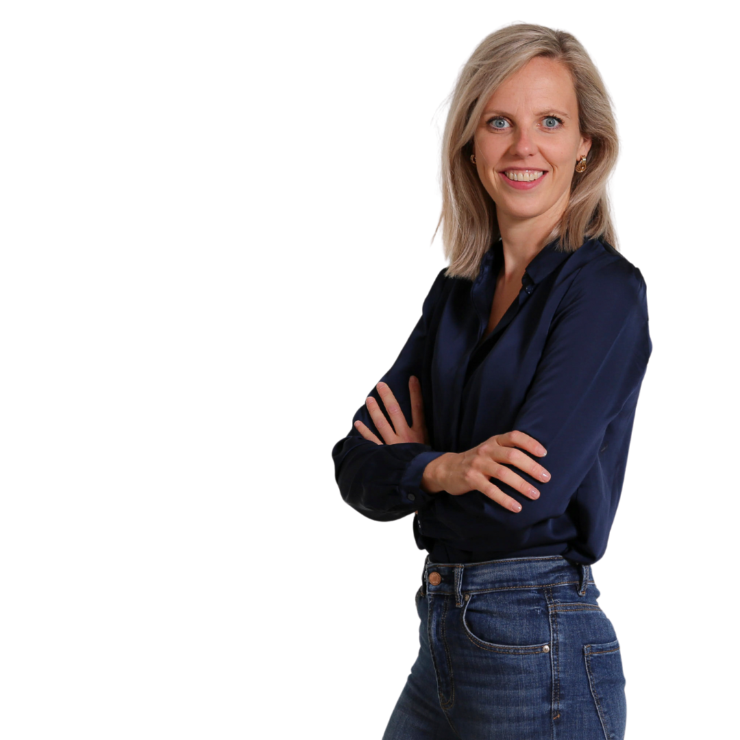 Vrouw staat met haar armen over elkaar, gekleed in een donkerblauwe blouse en jeans, tegen een witte achtergrond.